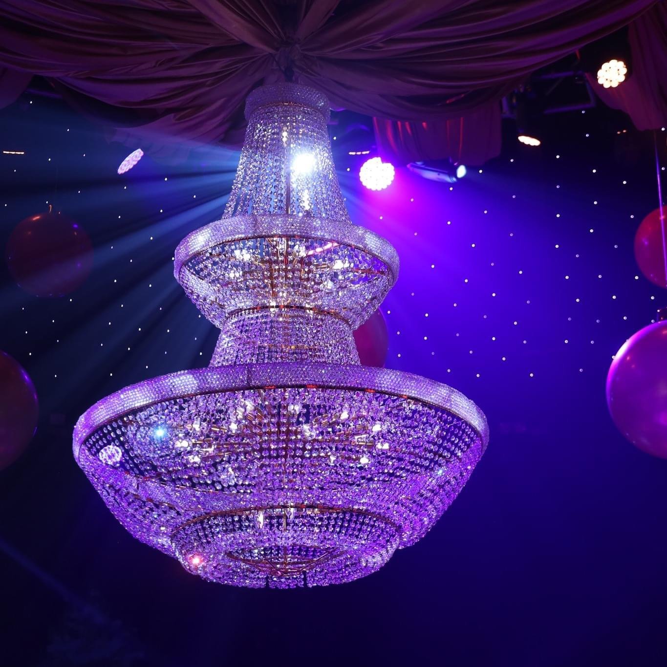 The surrounding darkness, dotted with tiny points of light, makes the chandelier feel almost celestial—grand, theatrical, and slightly surreal.