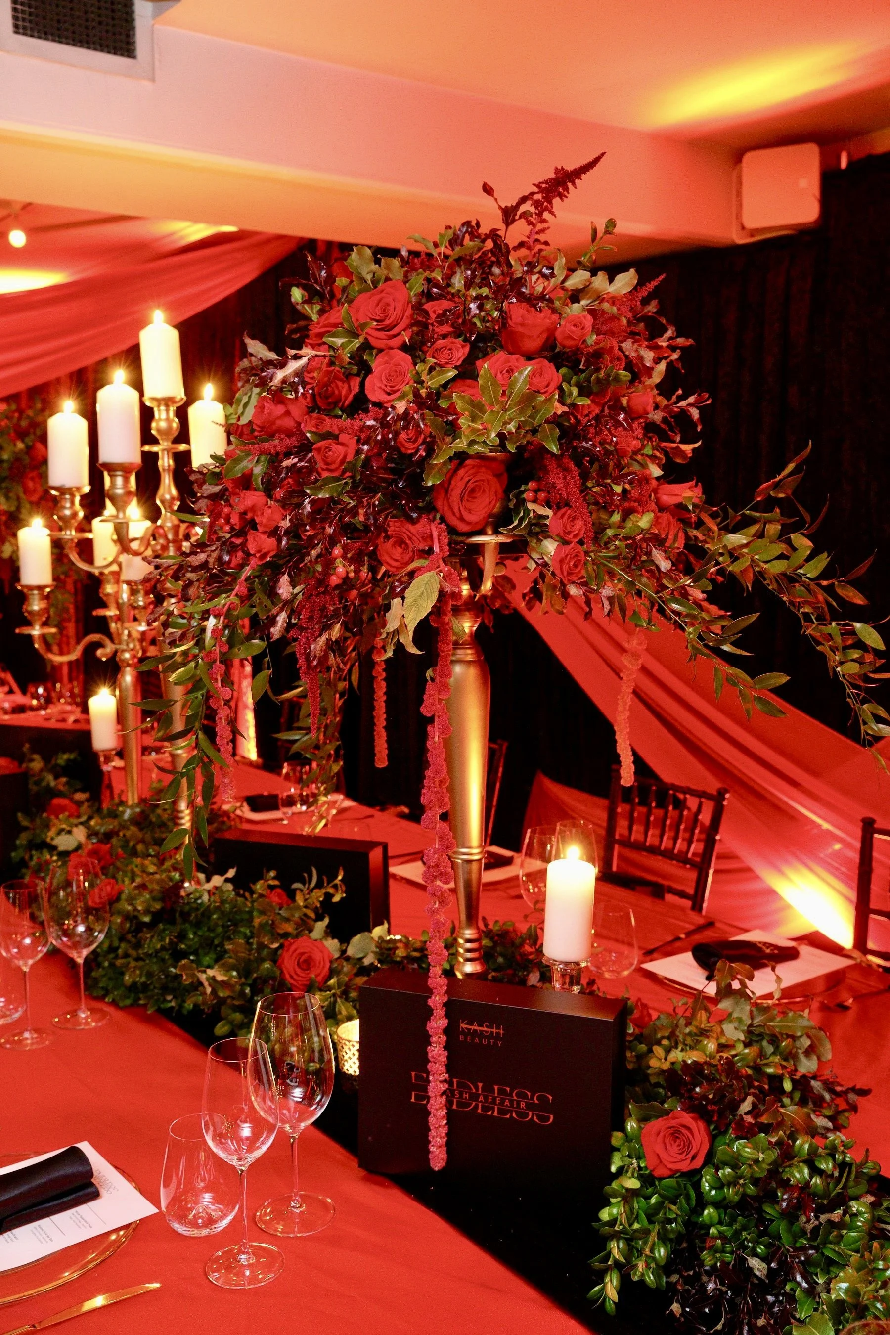 Deep red draping and warm golden uplighting wrap the walls, creating an opulent, almost cabaret‑style atmosphere.