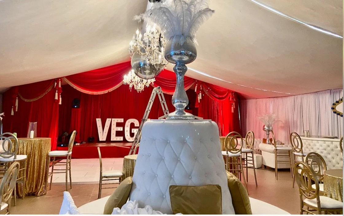 Decorated event space with gold chairs, elegant tables, and a stage with large 'VEG' letters and a ladder in the background.