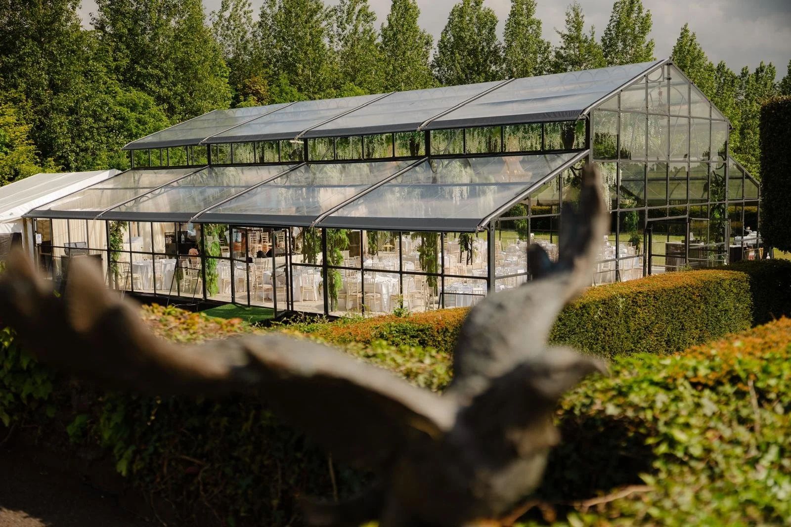 Grand crystal chandeliers glow warmly, framed by cascades of trailing white florals and greenery that soften the black metal framework and create a romantic, conservatory atmosphere.