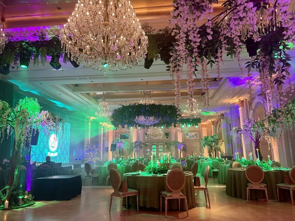 Elegant banquet hall decorated with chandeliers, colorful lighting, and floral centerpieces.