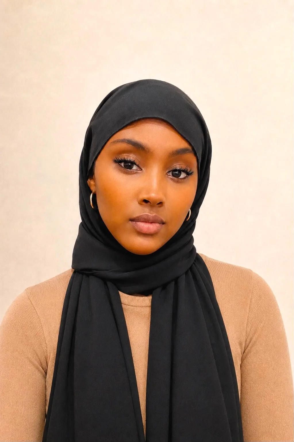 Young woman wearing a beige hijab and a maroon top, looking at the camera with a neutral expression.