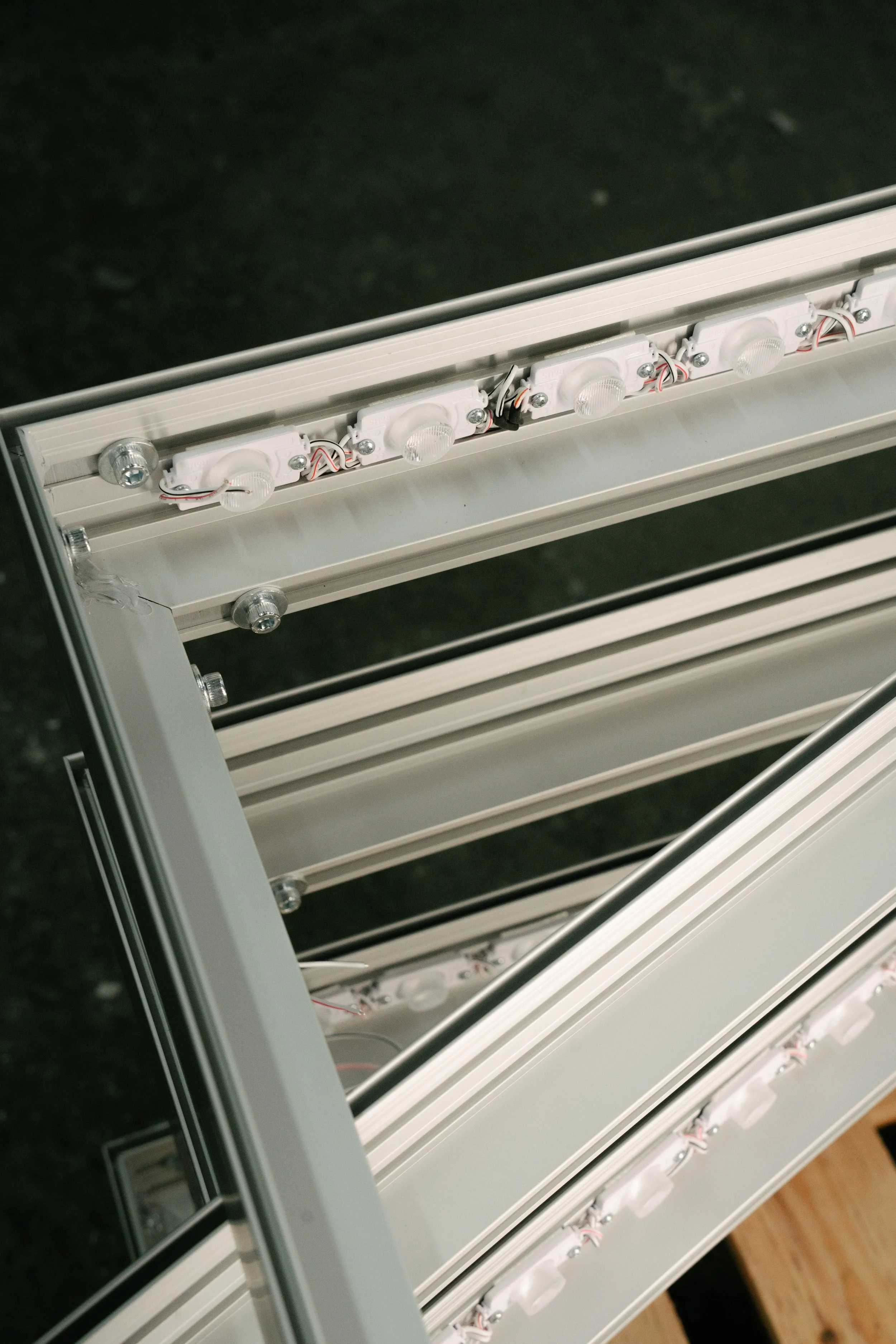 Close-up of an LED strip light inside a white aluminum frame with screws, wires, and light modules, on a black background.