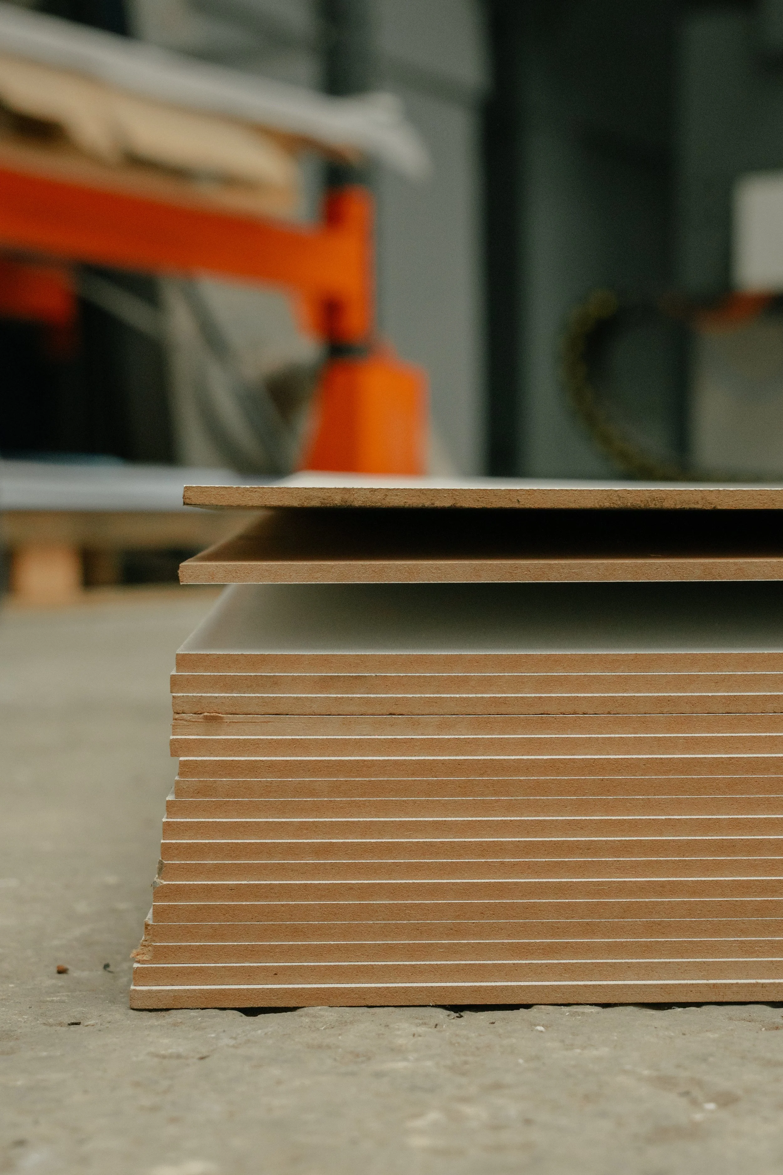 Stack of unfinished wooden planks on a rough concrete floor in a workshop or construction area.