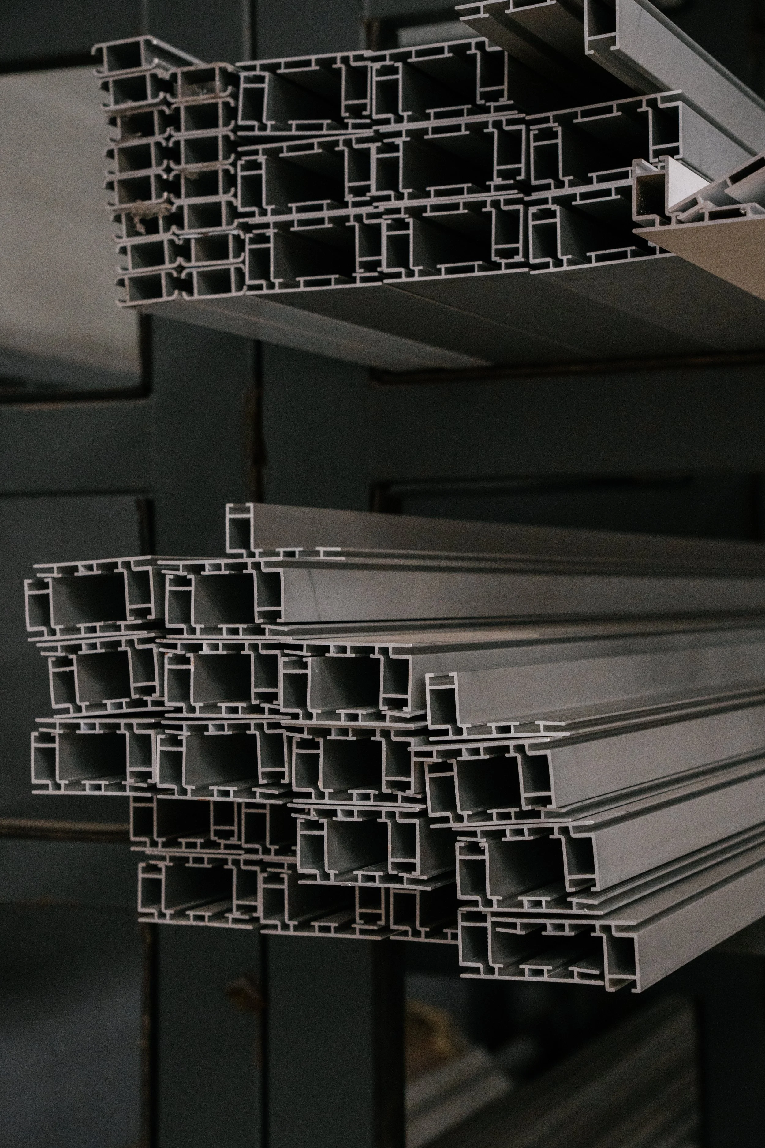 Stacks of metal or aluminum rectangular tubing with hollow centers, stored on racks in an industrial or warehouse setting.