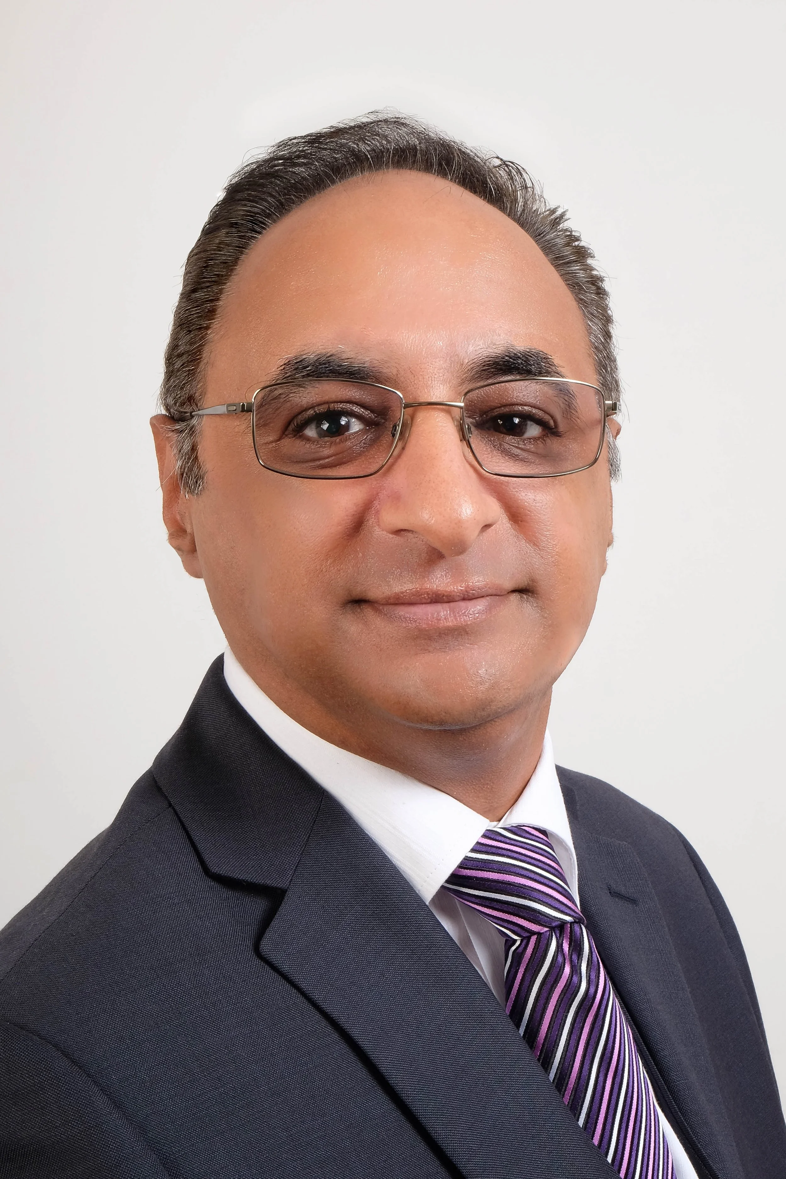A professional man in a suit and tie wears glasses, looking directly at the camera with a neutral expression.