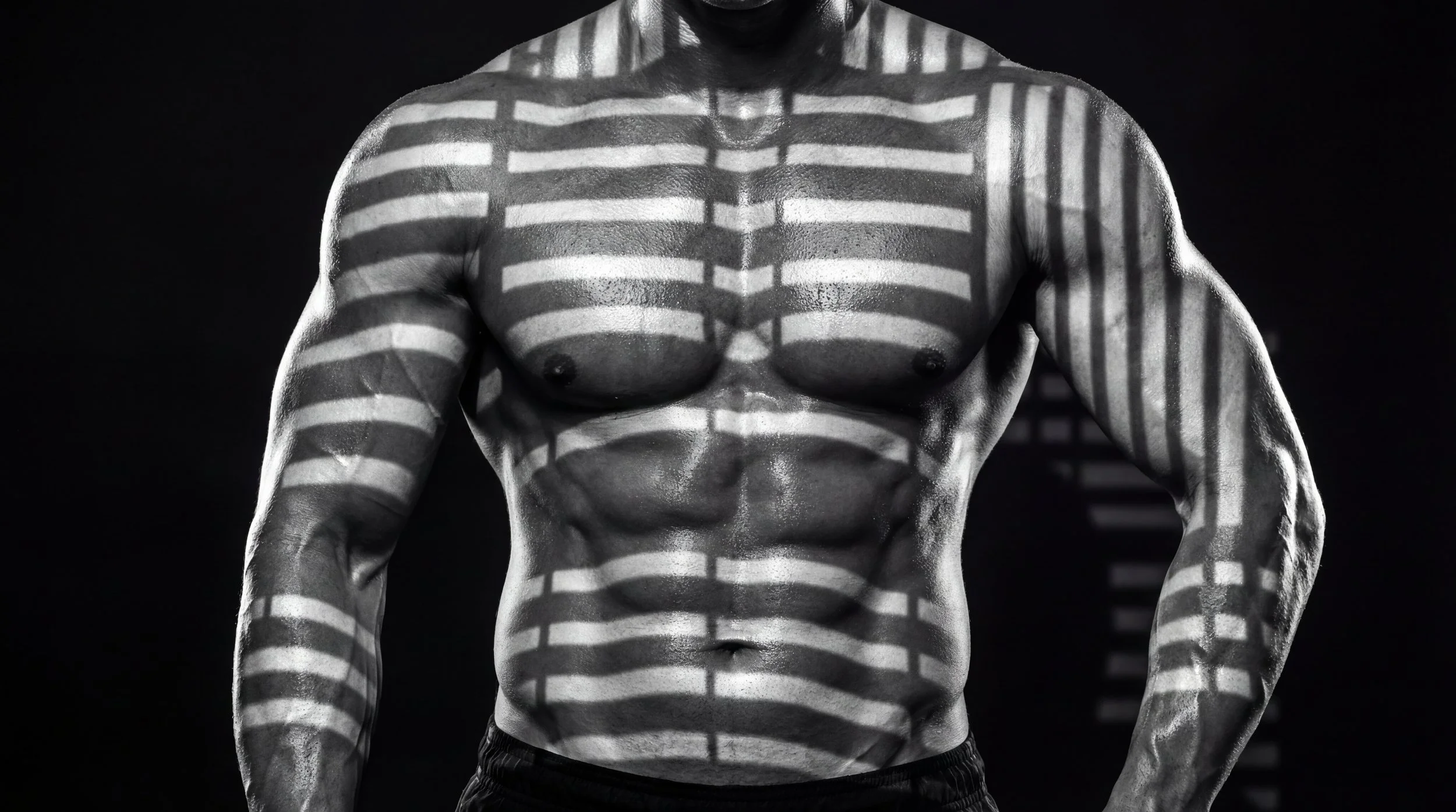Black and white photo of a muscular man's upper body with horizontal blinds casting shadows across his torso and arms.