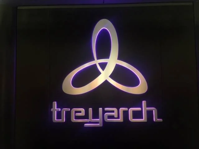 Neon sign displaying a three interlocking loops symbol and the word "treyarch" in purple and white on a black background.