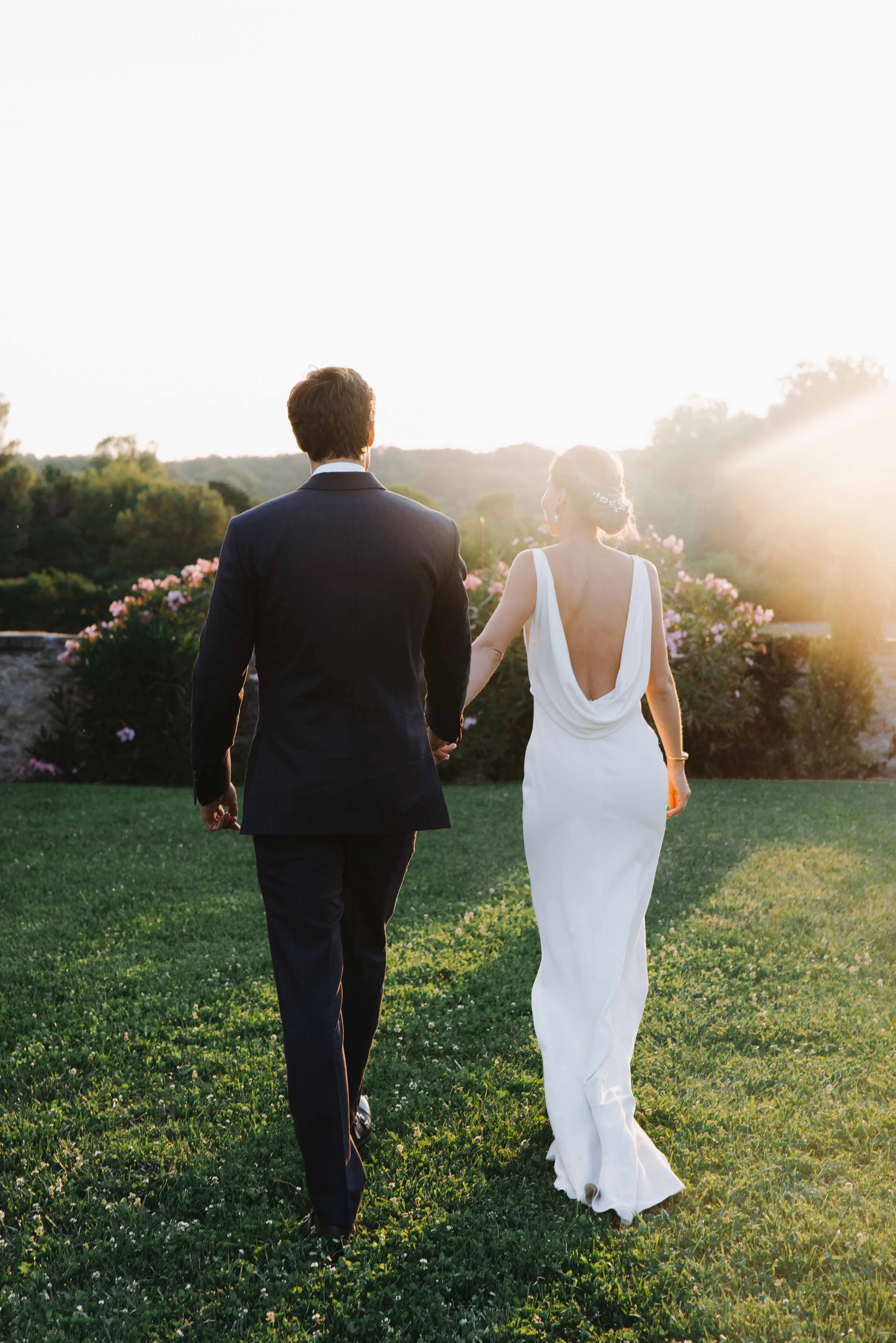 Un couple en tenue de mariage qui marche dans un jardin verdoyant au coucher du soleil.
