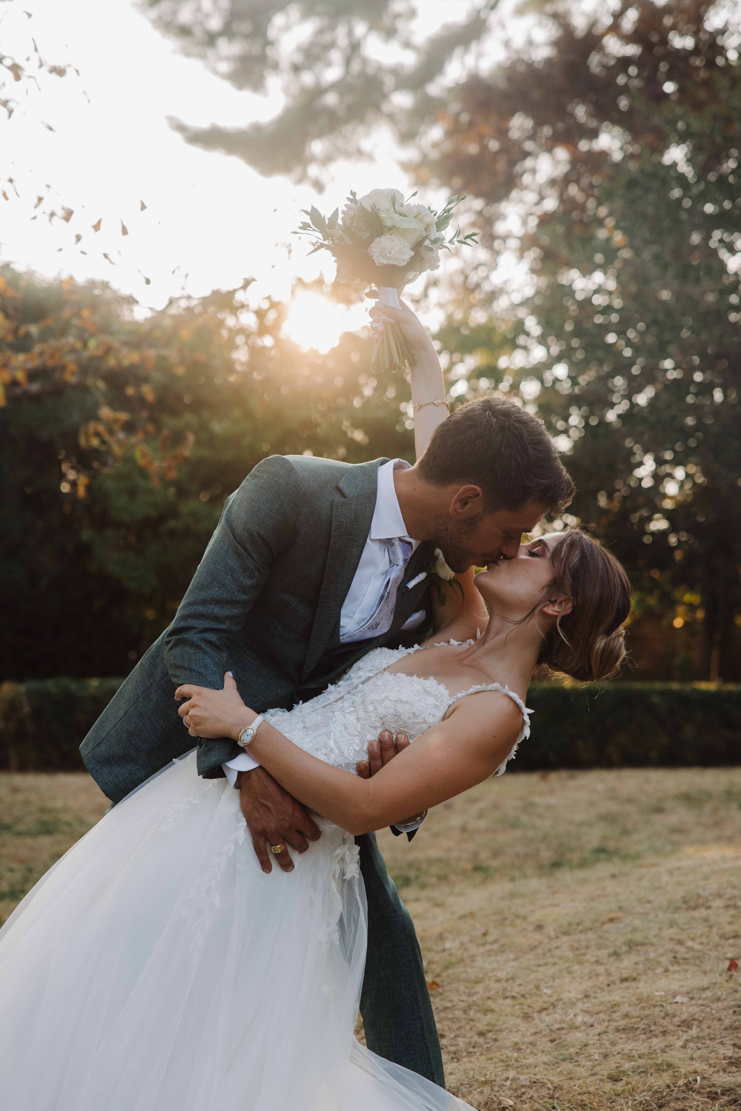 Un couple en costume de mariage, en train de s'embrasser dans un parc lors d'une séance photo en soirée.
