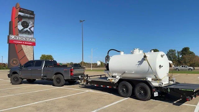 A black pickup truck towing a large white tank on a trailer in a parking lot with a Choctaw Casino & Resort sign in the background.