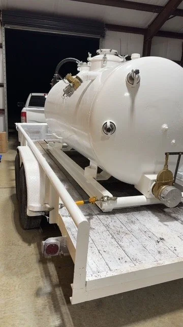 A large white cylindrical tank mounted on a flatbed trailer in a storage or workshop setting.