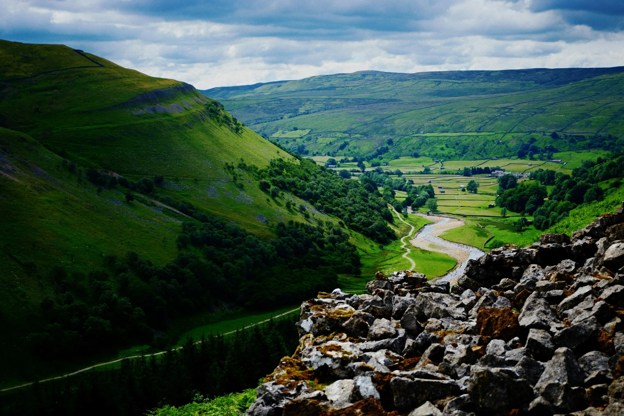 Green valley in the mountains with a river flowing through and a rocky foreground.