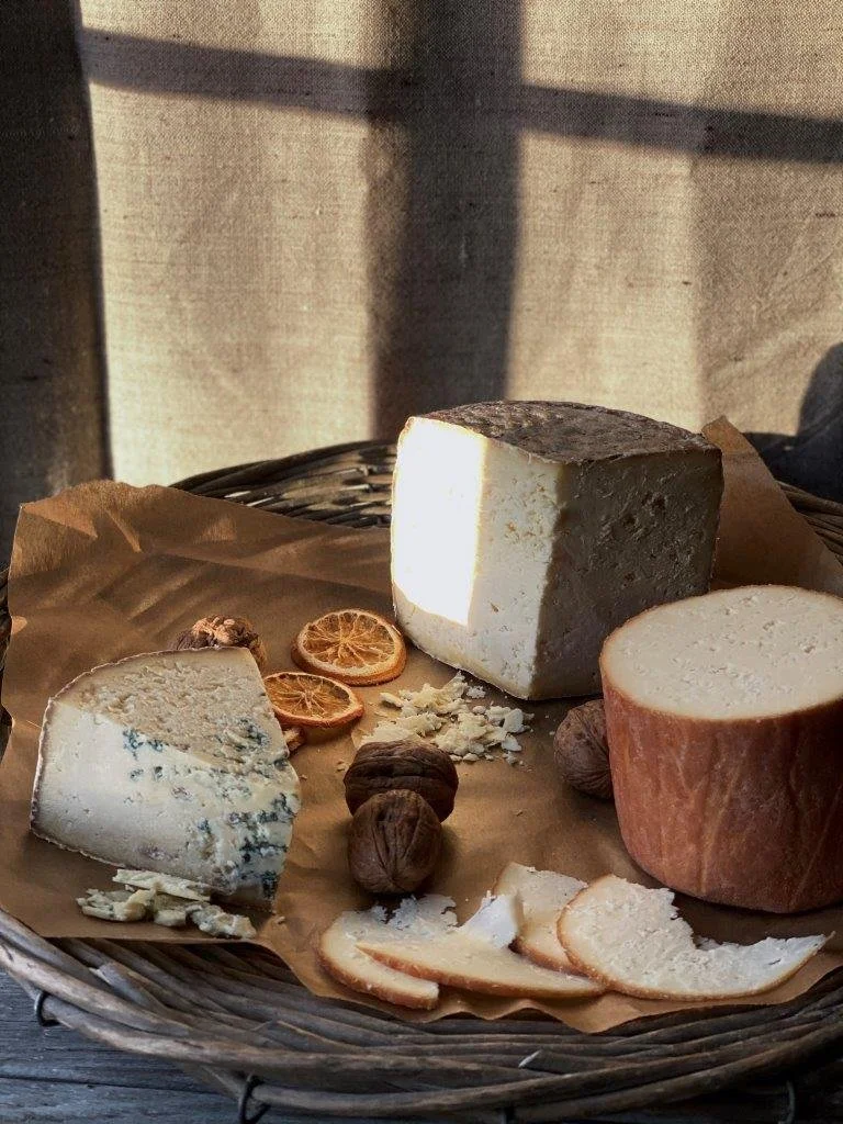 A wicker basket with cheese, walnuts, and dried orange slices, lit by sunlight.