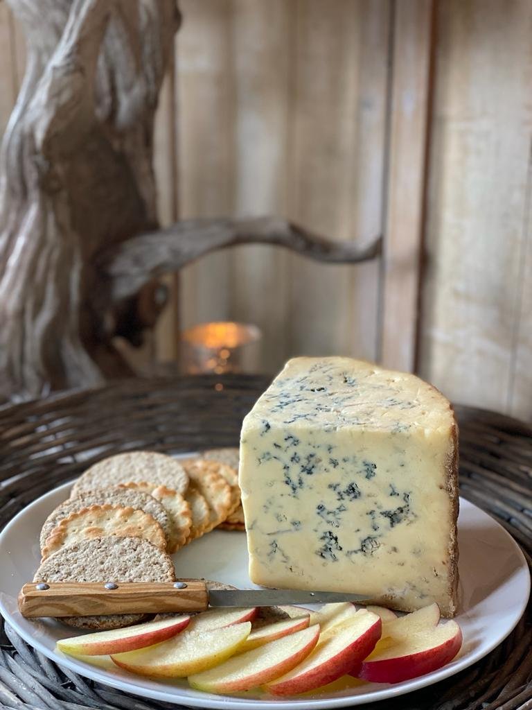 A wedge of blue cheese on a white plate, with apple slices and crackers, in a rustic setting