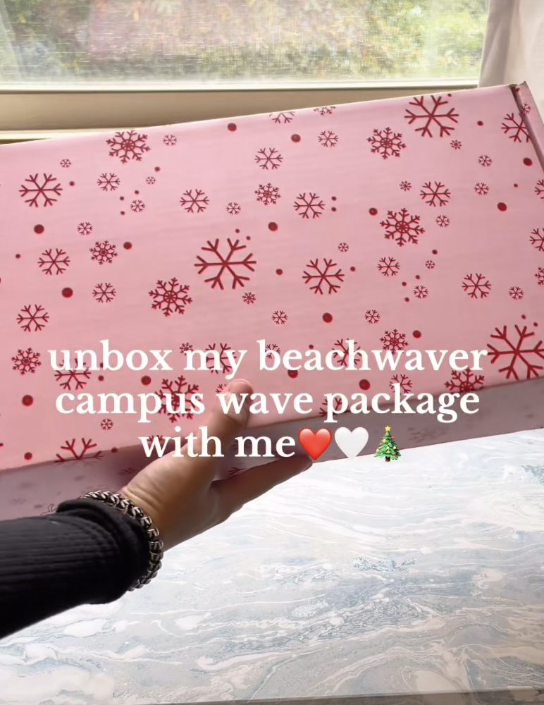 Person holding a pink box with red snowflake patterns near a window, with water and sky visible outside.