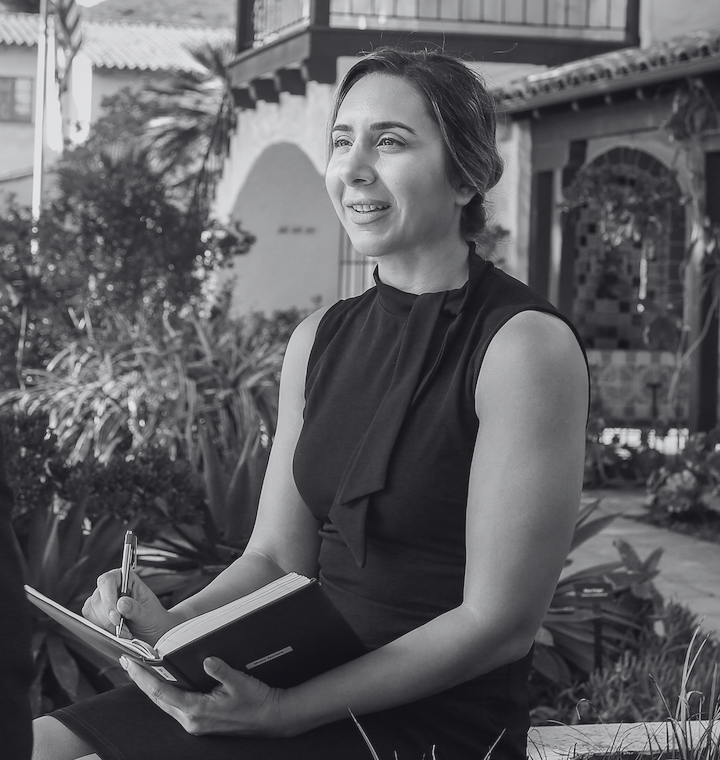 A woman sitting holding a pen and notes in black dress