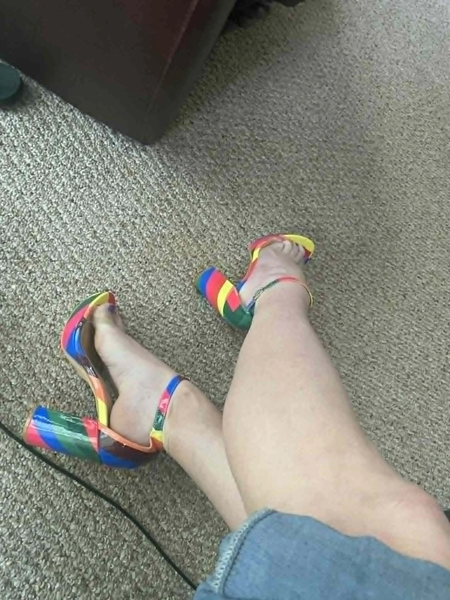 Person wearing colorful striped high heel shoes sitting on beige carpeted floor