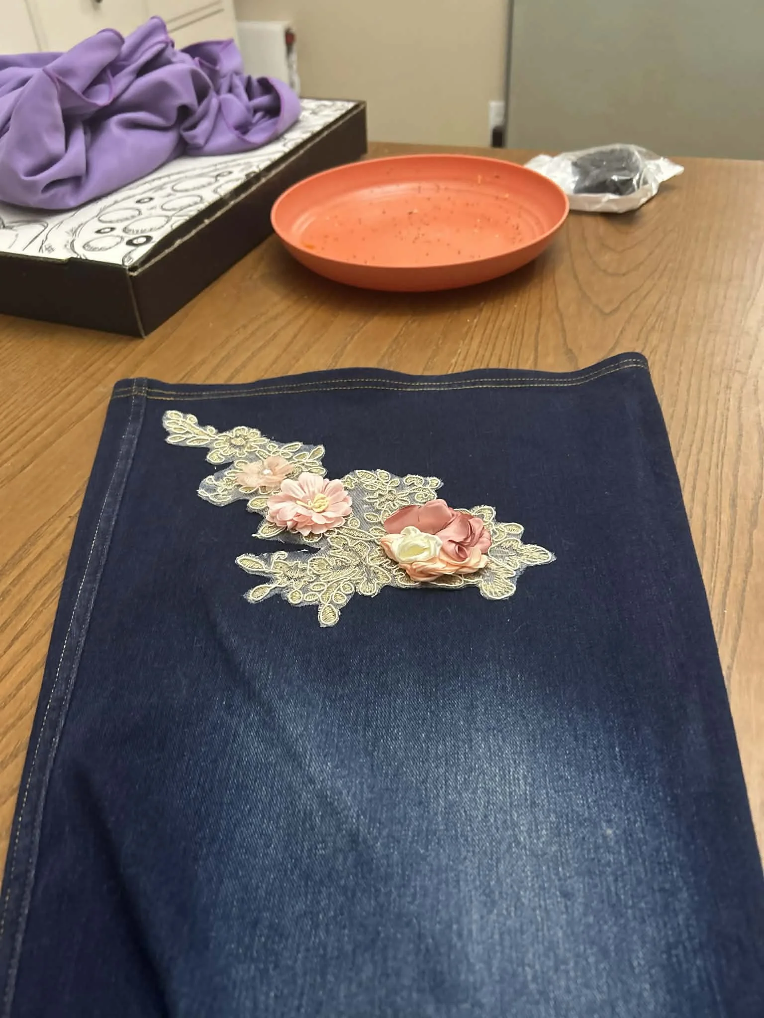 Close-up of dark blue denim jeans with floral embroidery, laid out on a wooden table.