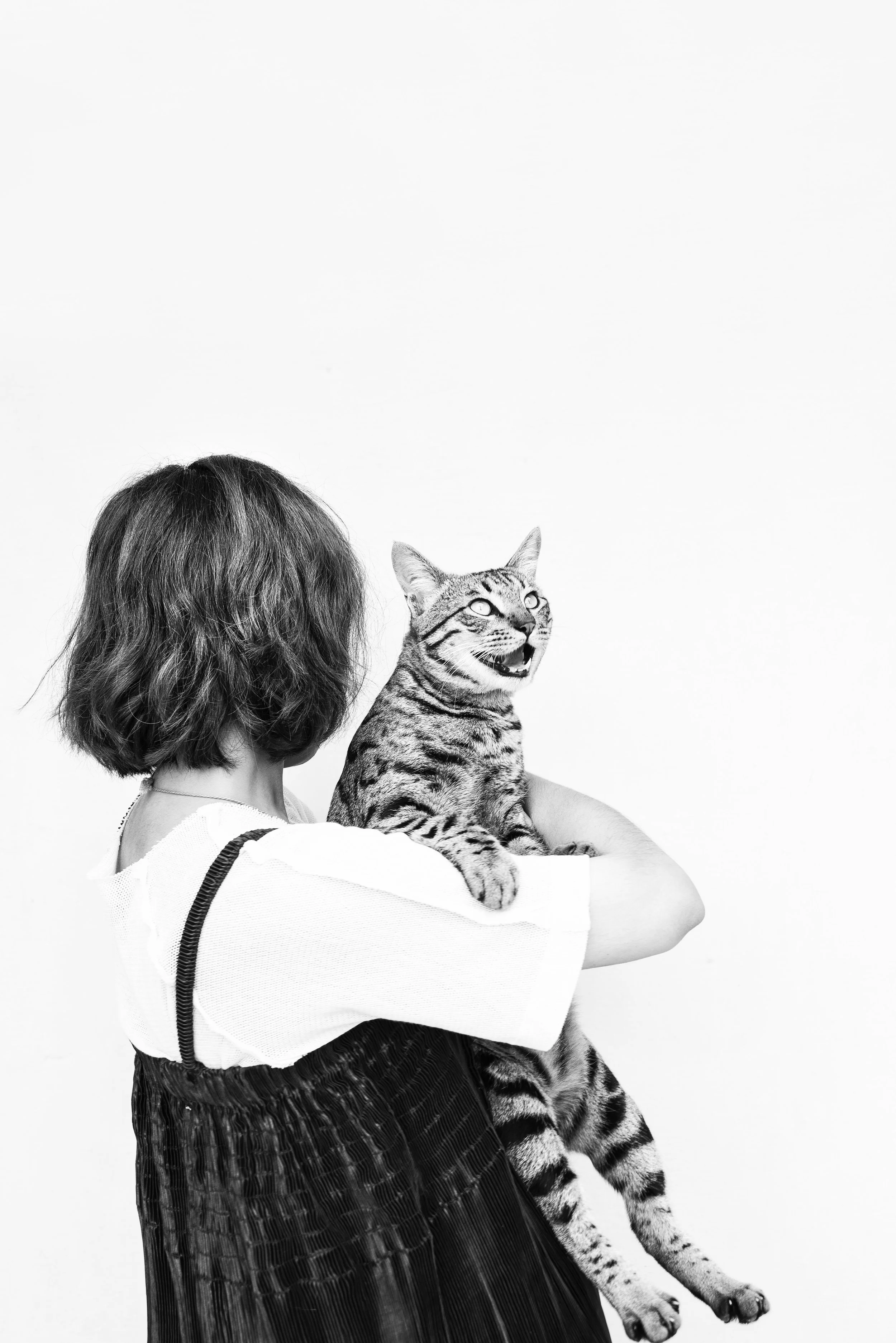 Person holding a tabby cat, facing away from the camera, in a black-and-white photo against a plain white background.