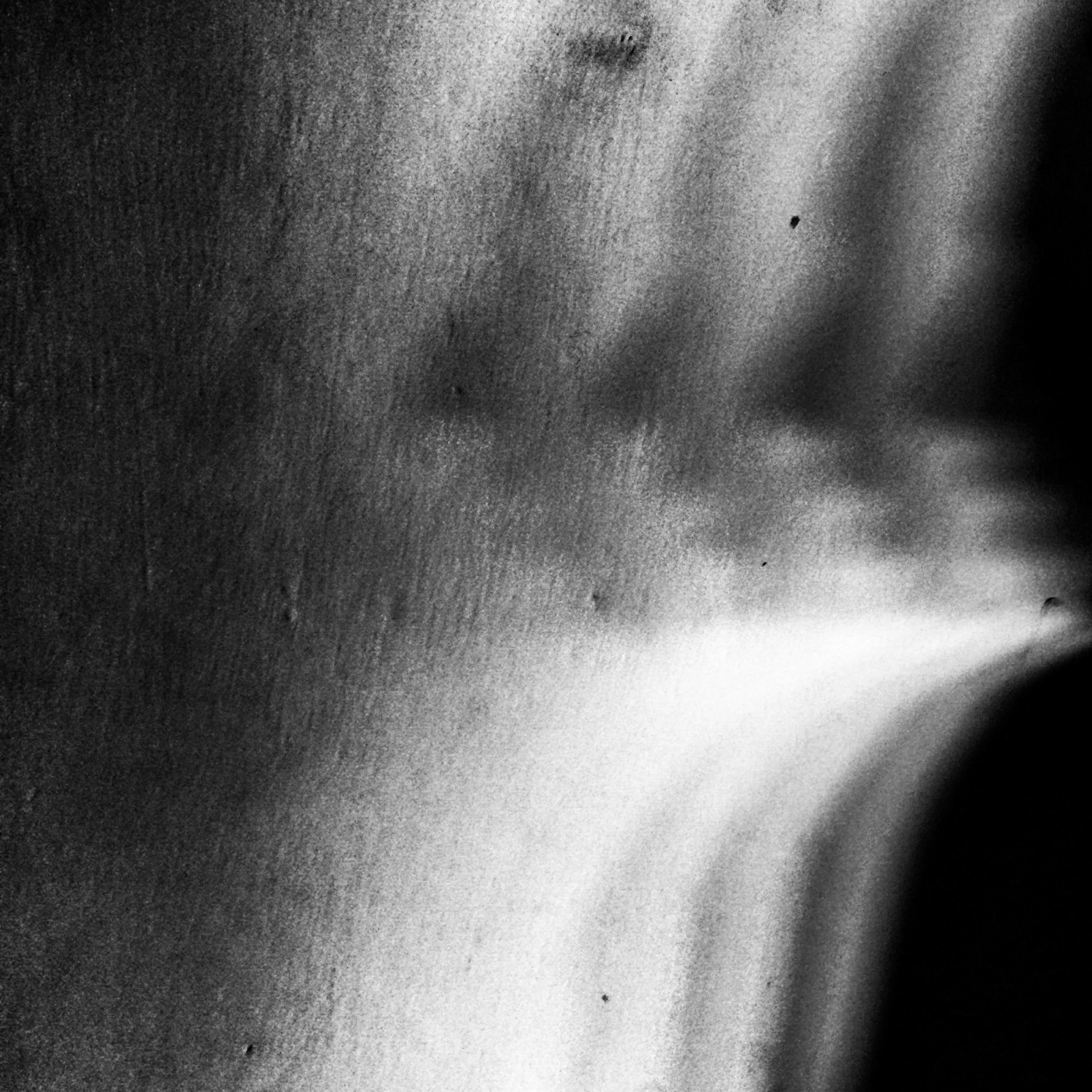 Close-up black-and-white photograph of a textured surface, possibly a wall or object with shadows and light creating abstract patterns.