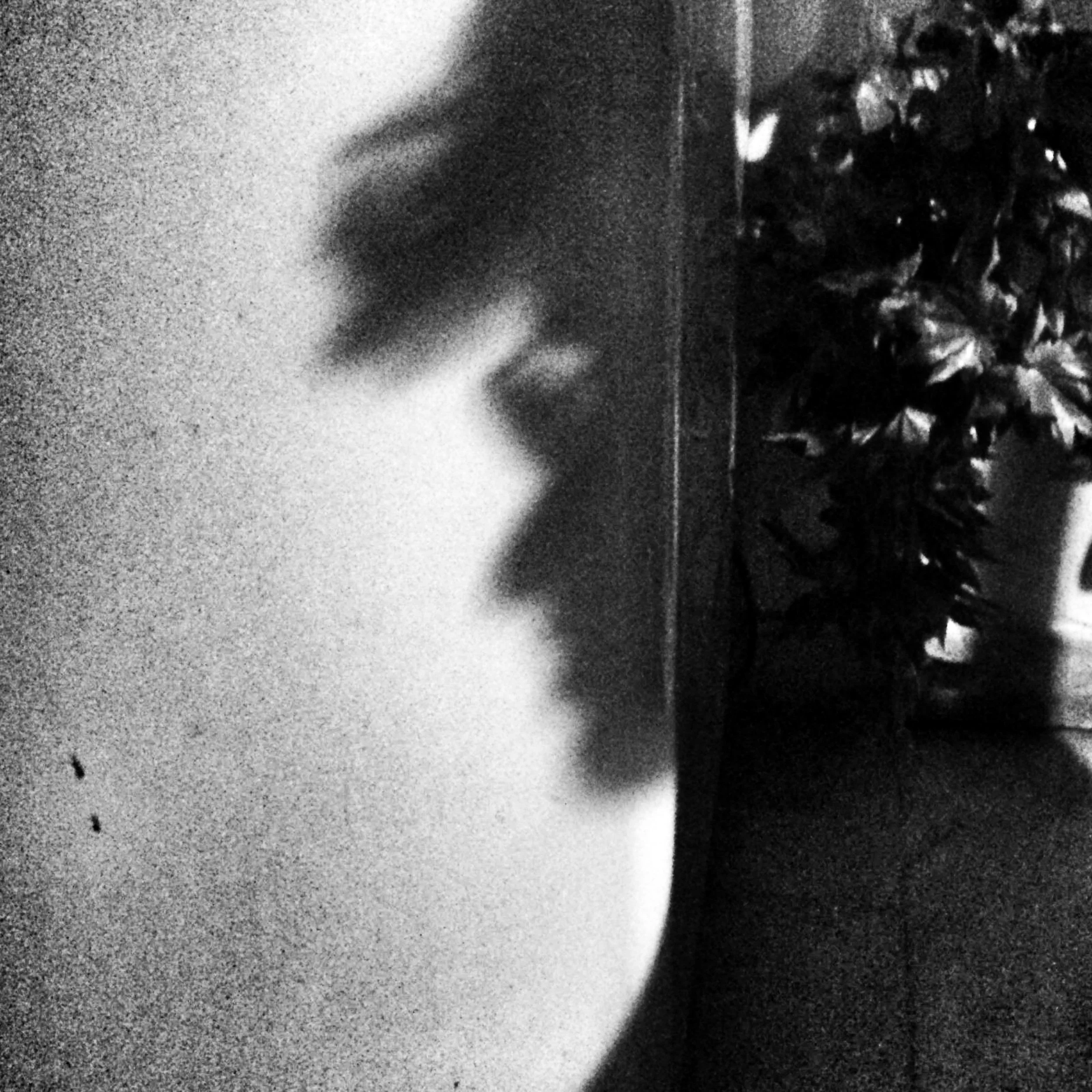 Close-up of a person's lips, black and white photo with a grainy texture, with some foliage in the background.