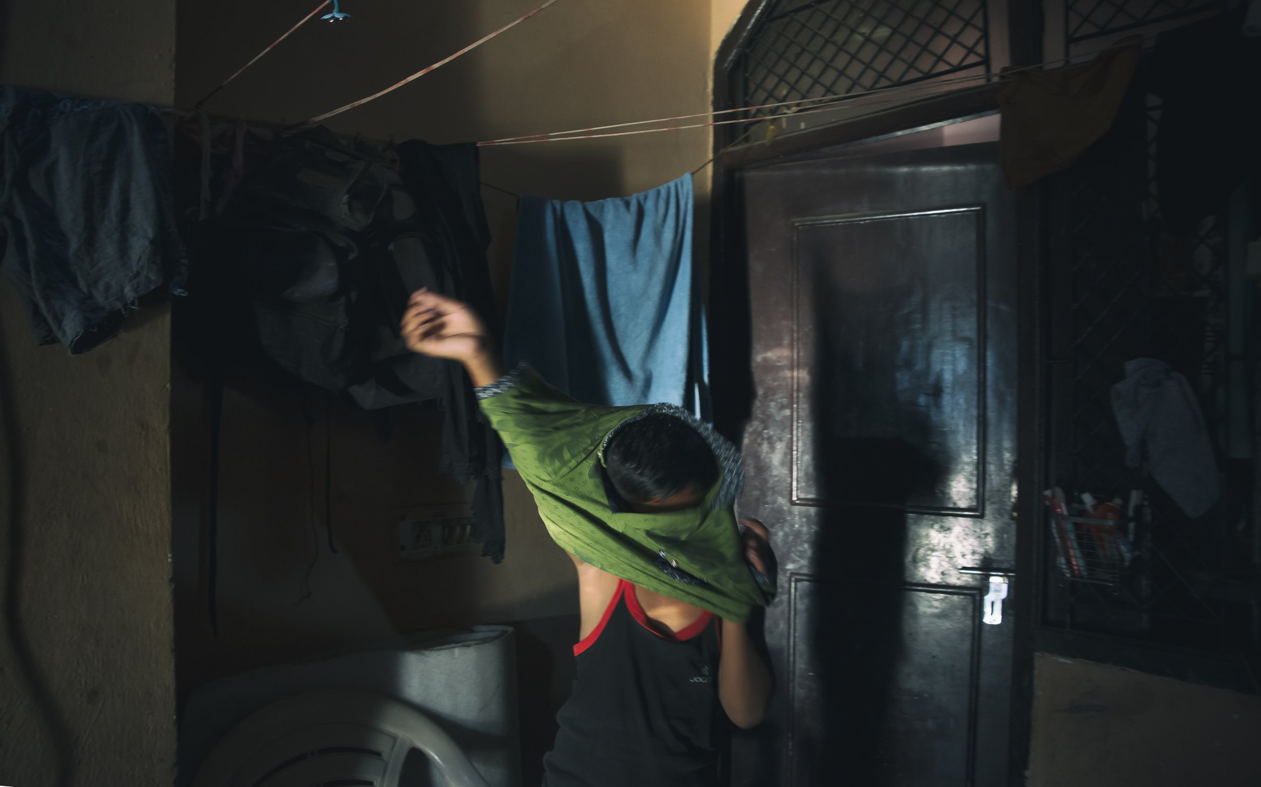 Two people fighting on the floor of a small room, with laundry hanging on a line overhead.