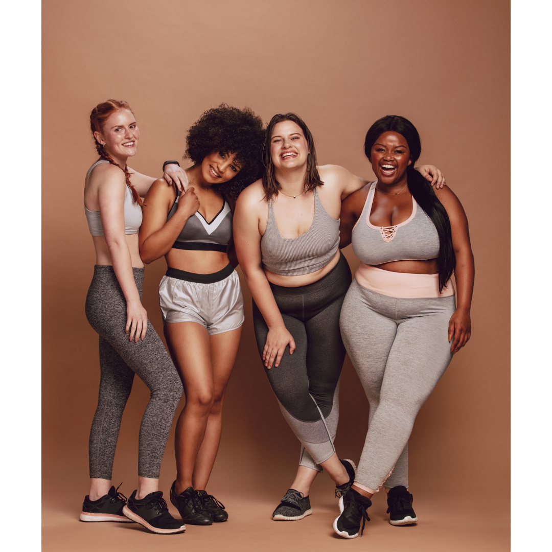Group of four diverse women in athletic wear smiling and laughing together against a plain brown background.