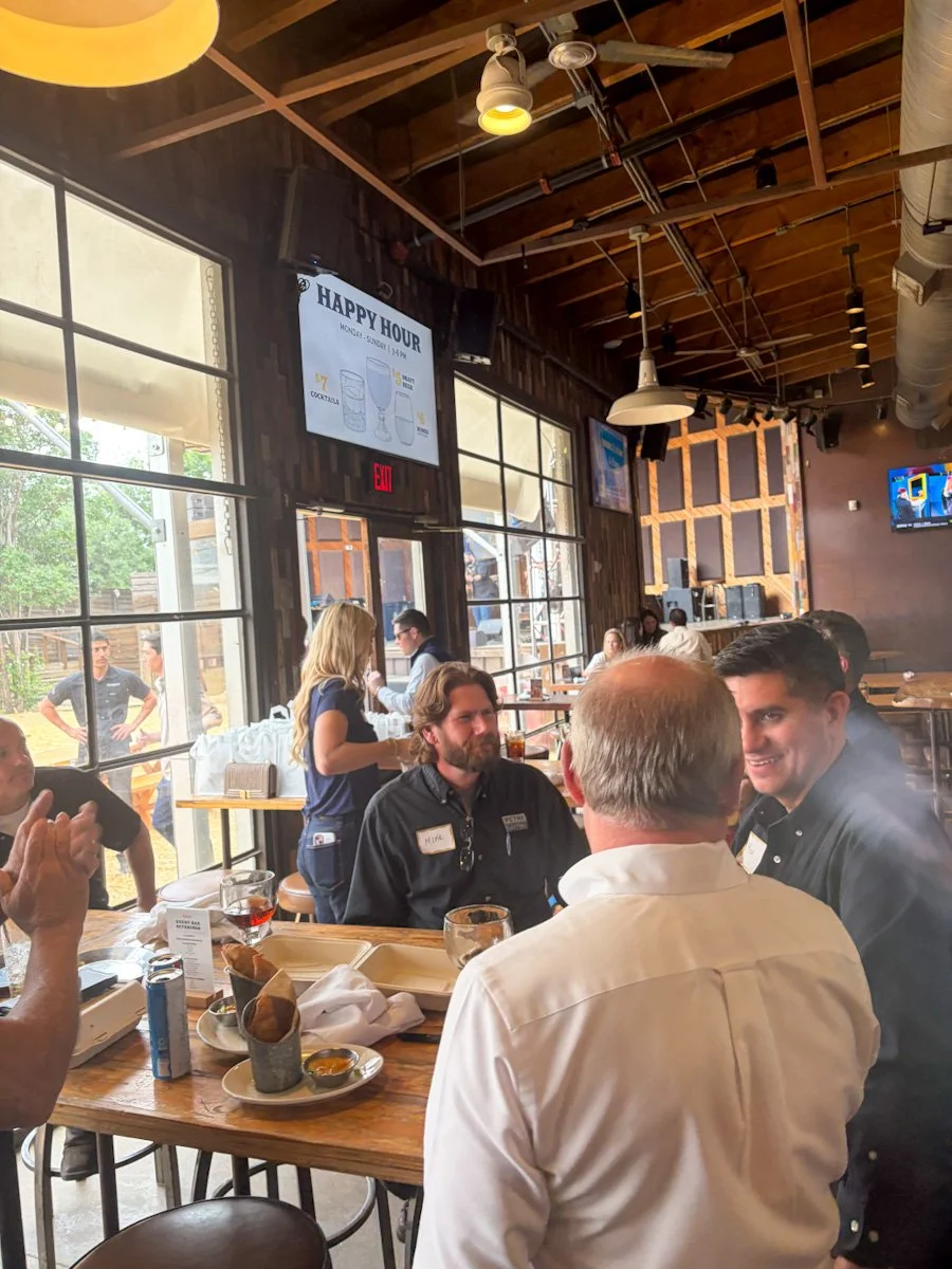 Indoor restaurant scene with people sitting at tables, large windows, and a TV on the wall.