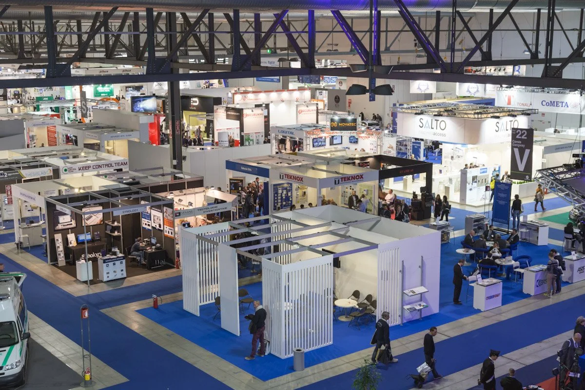 Trade show exhibiting various booths and displays with attendees walking around and sitting at tables.