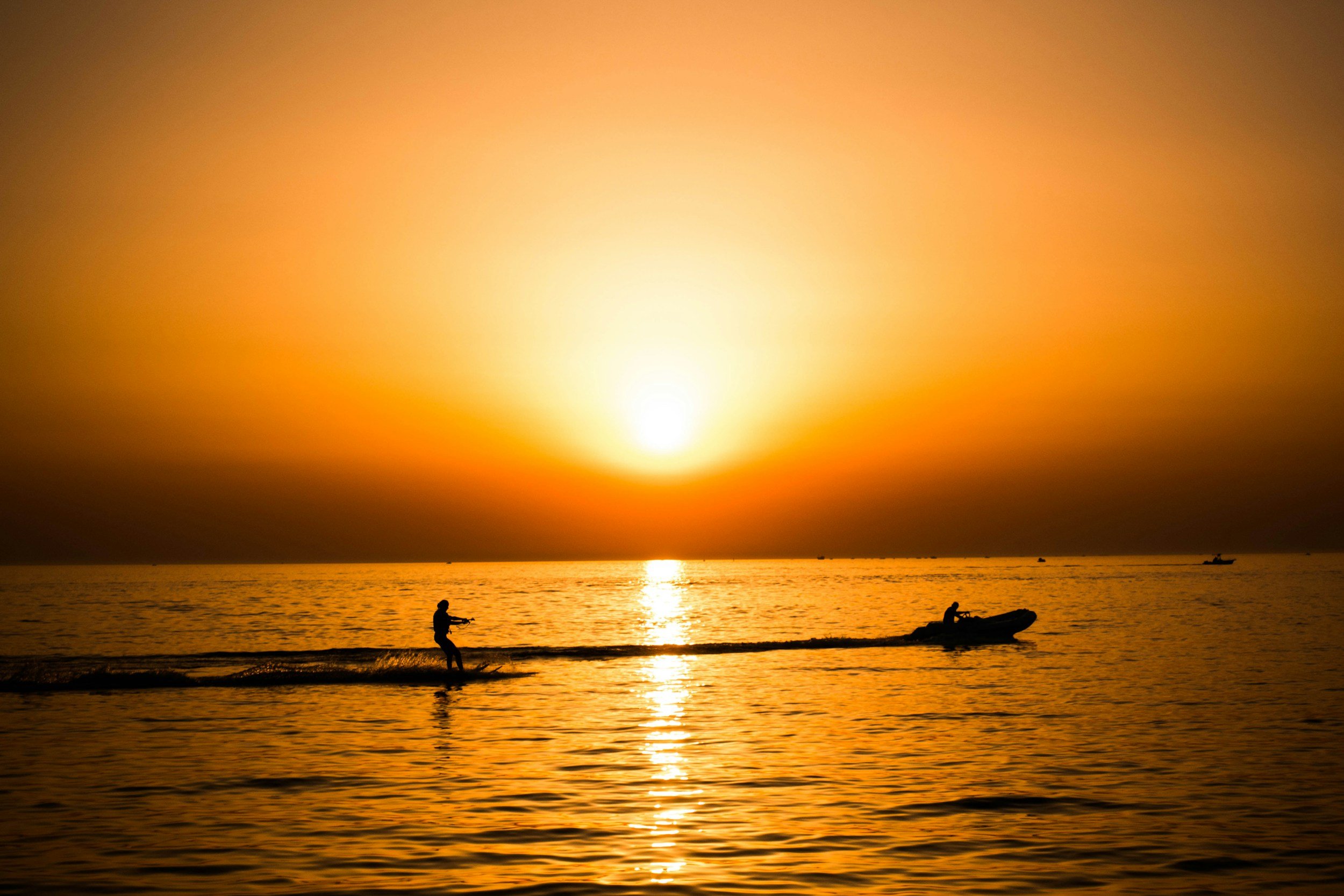 Silhouette von zwei Menschen beim Wasserski und Boot bei Sonnenuntergang auf dem Meer