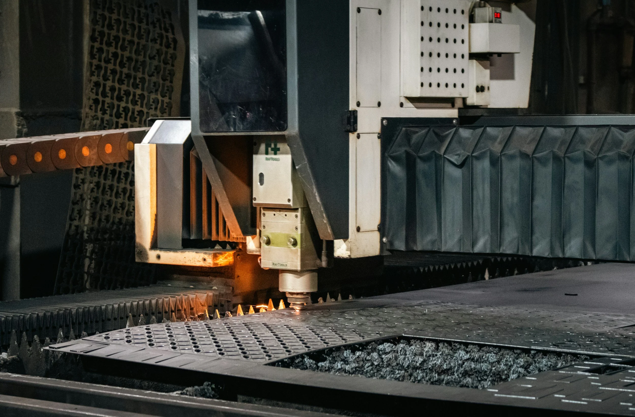 Close-up of a CNC laser cutting machine cutting metal, with sparks and flame visible at the cutting point.