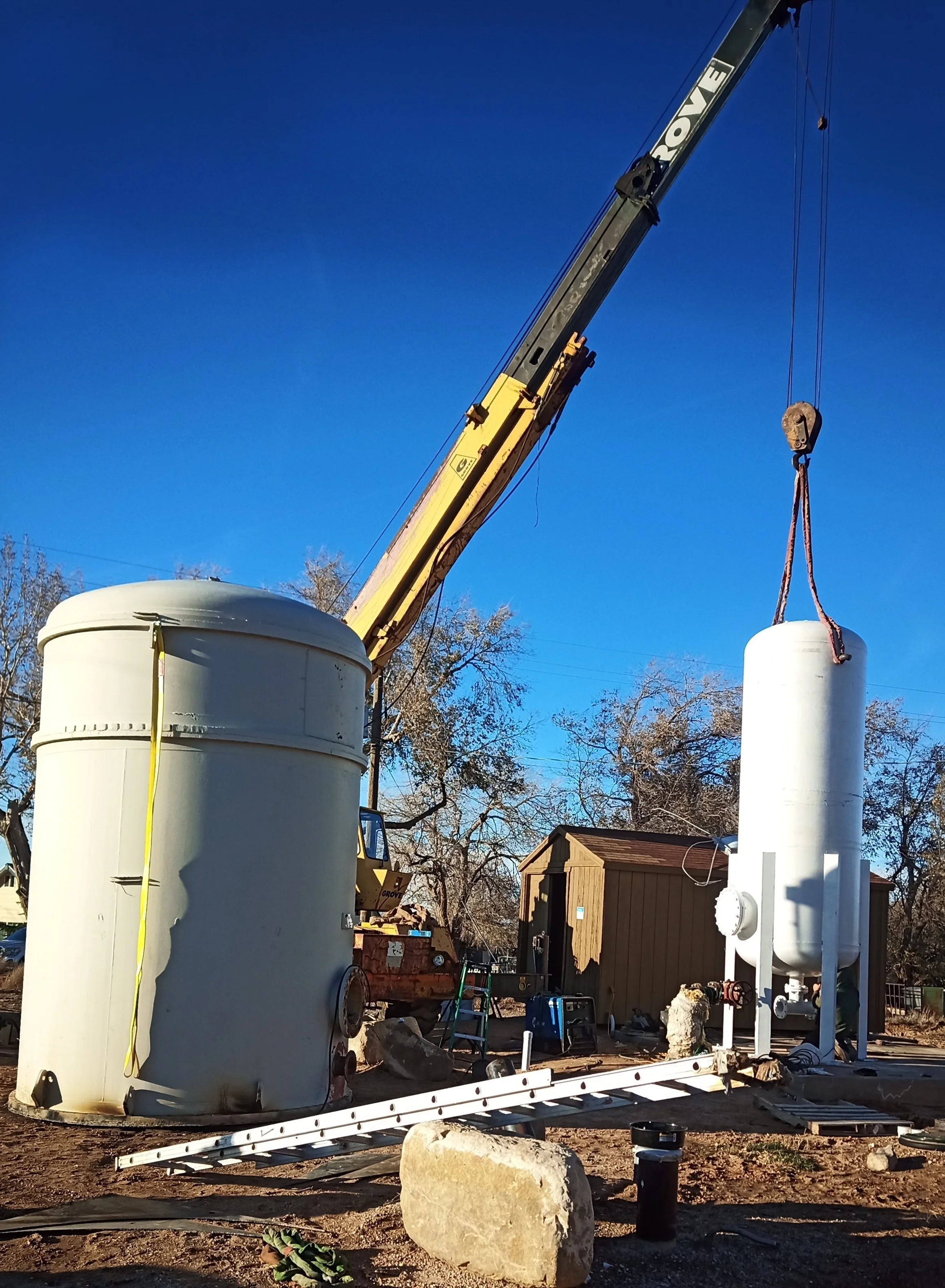 A mobile crane setting a custom vertical pressure vessel into place on an outdoor concrete foundation pad during a field installation project