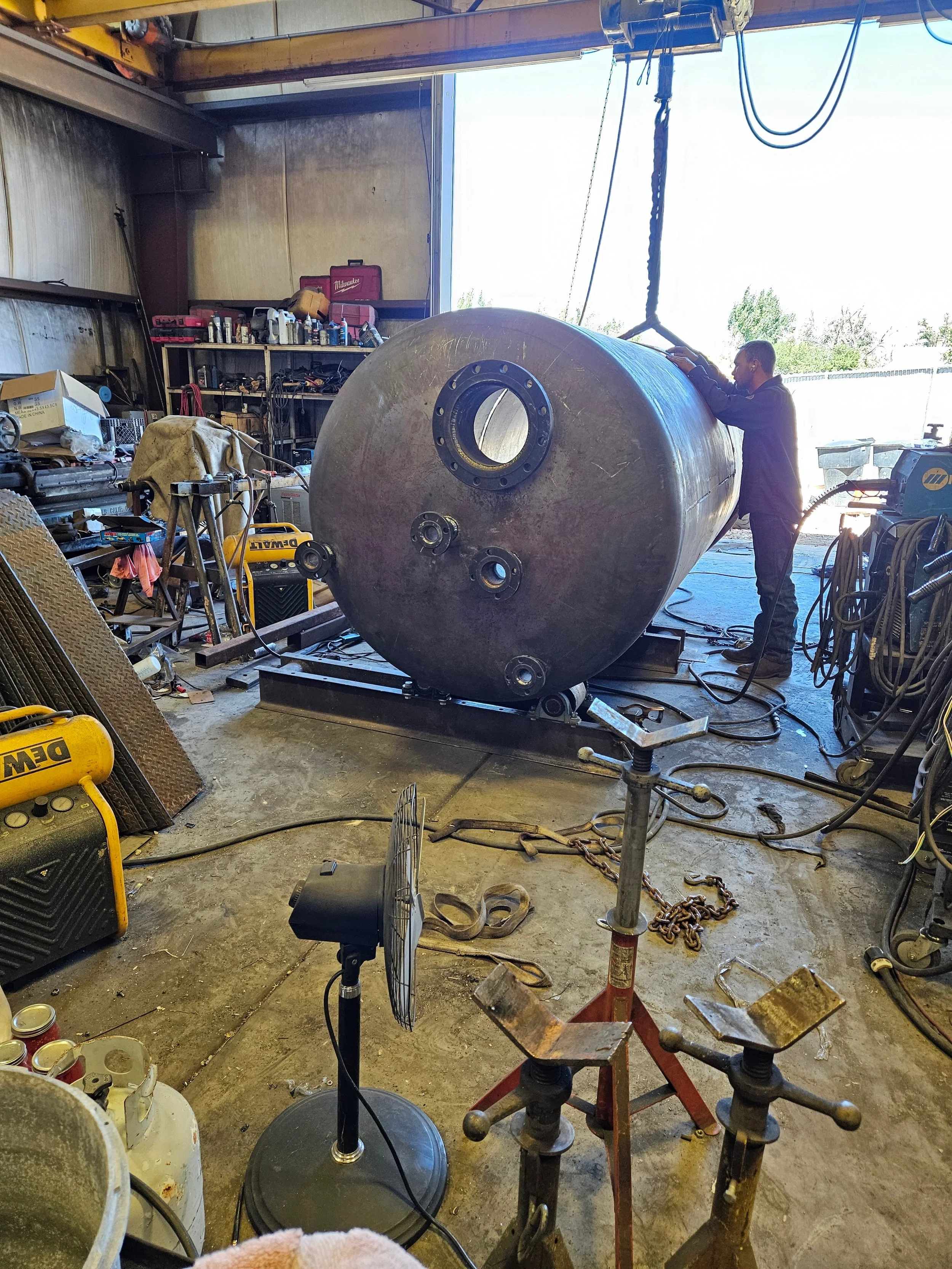 A Peak Welding technician inspecting nozzle fit-up on a large carbon steel ASME pressure vessel suspended by an overhead shop crane inside the Manti, Utah facility.