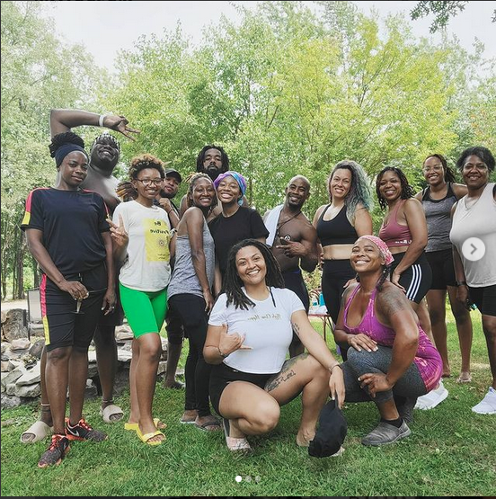 Group of diverse women and men smiling outdoors in a park with green trees in the background.