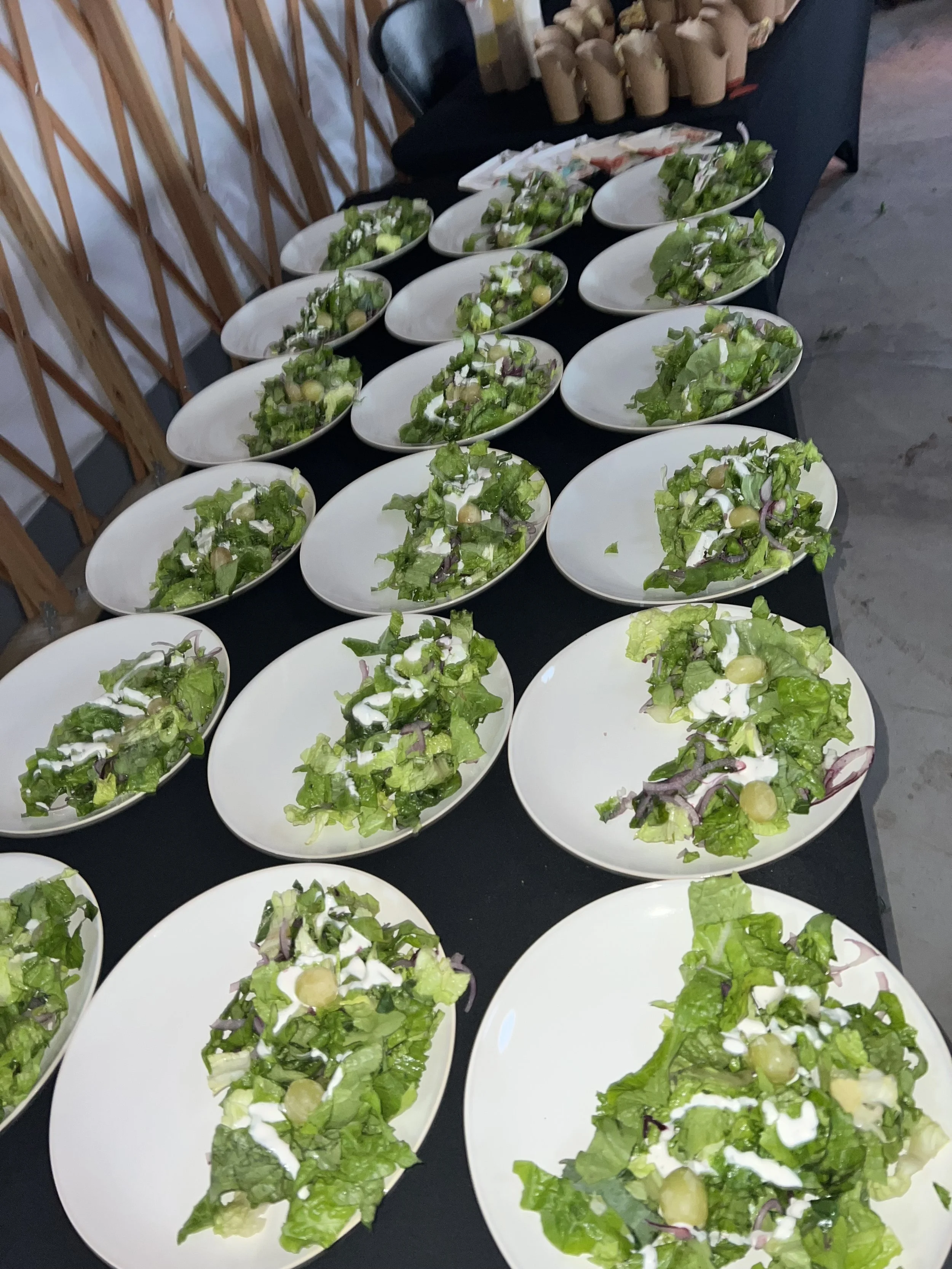Multiple plates of salad with greens, grapes, onions, and dressing arranged on a black table.