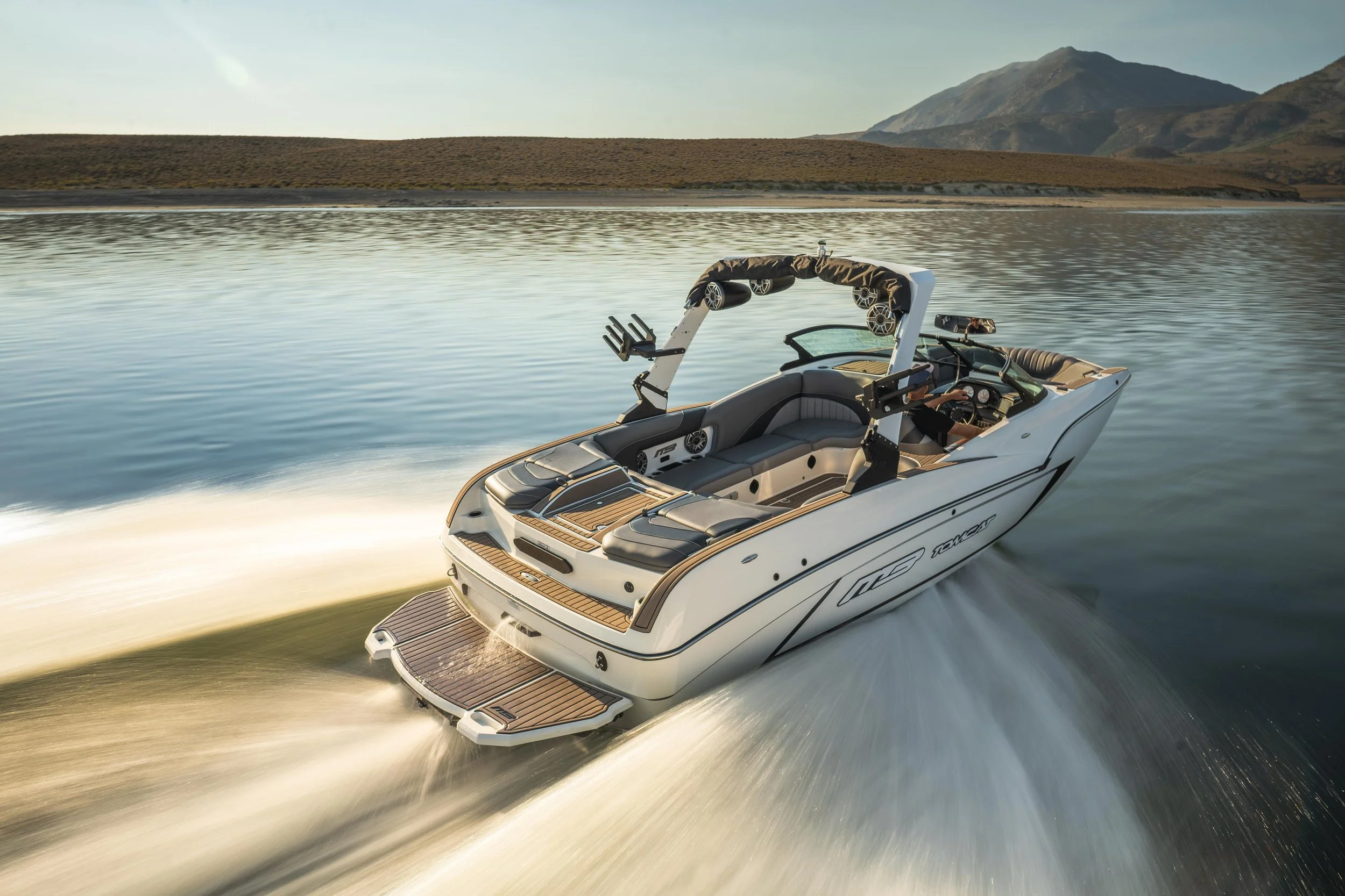 A modern motorboat moving quickly through a body of water, leaving a wake behind, with a mountainous landscape in the background.