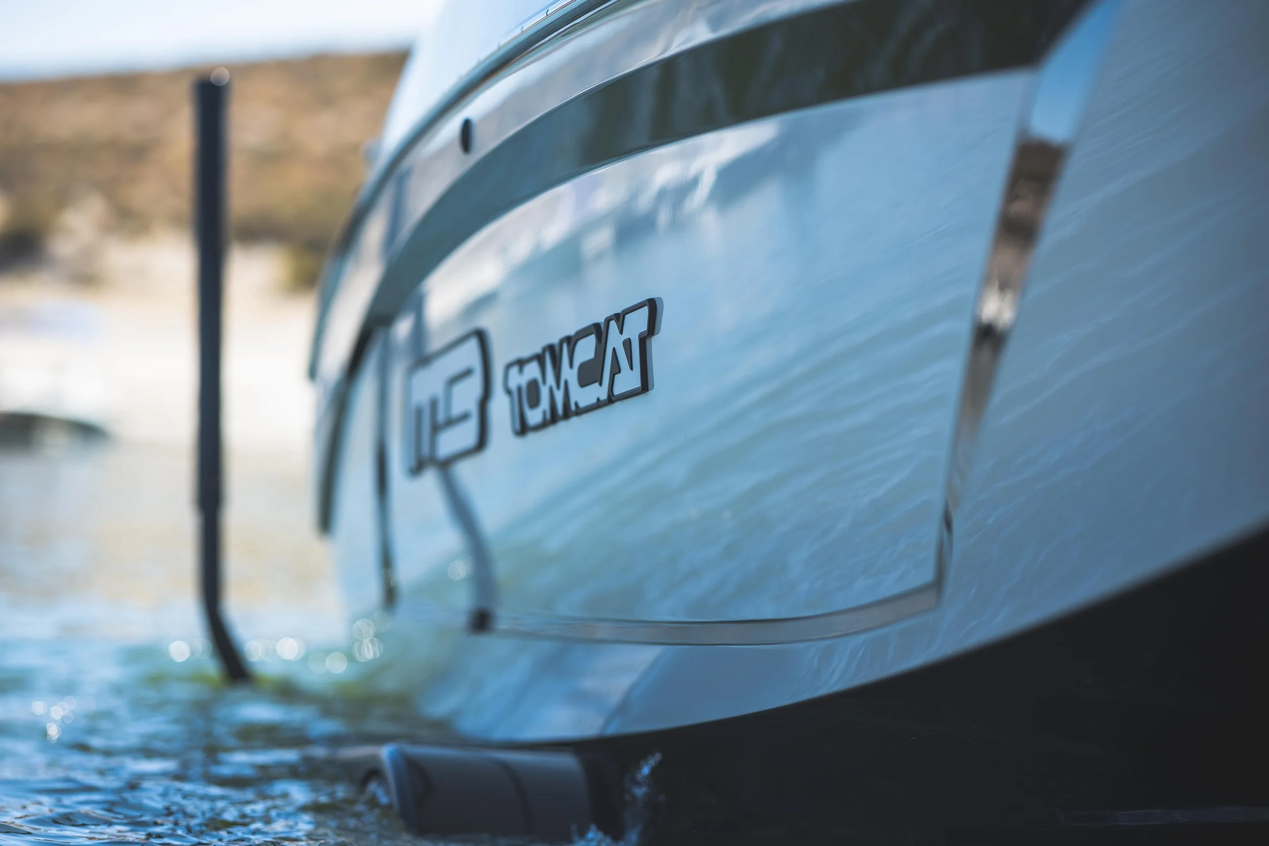 Close-up of a boat on water showing an Outboard engine logo and reflection, with a blurred shoreline in the background.