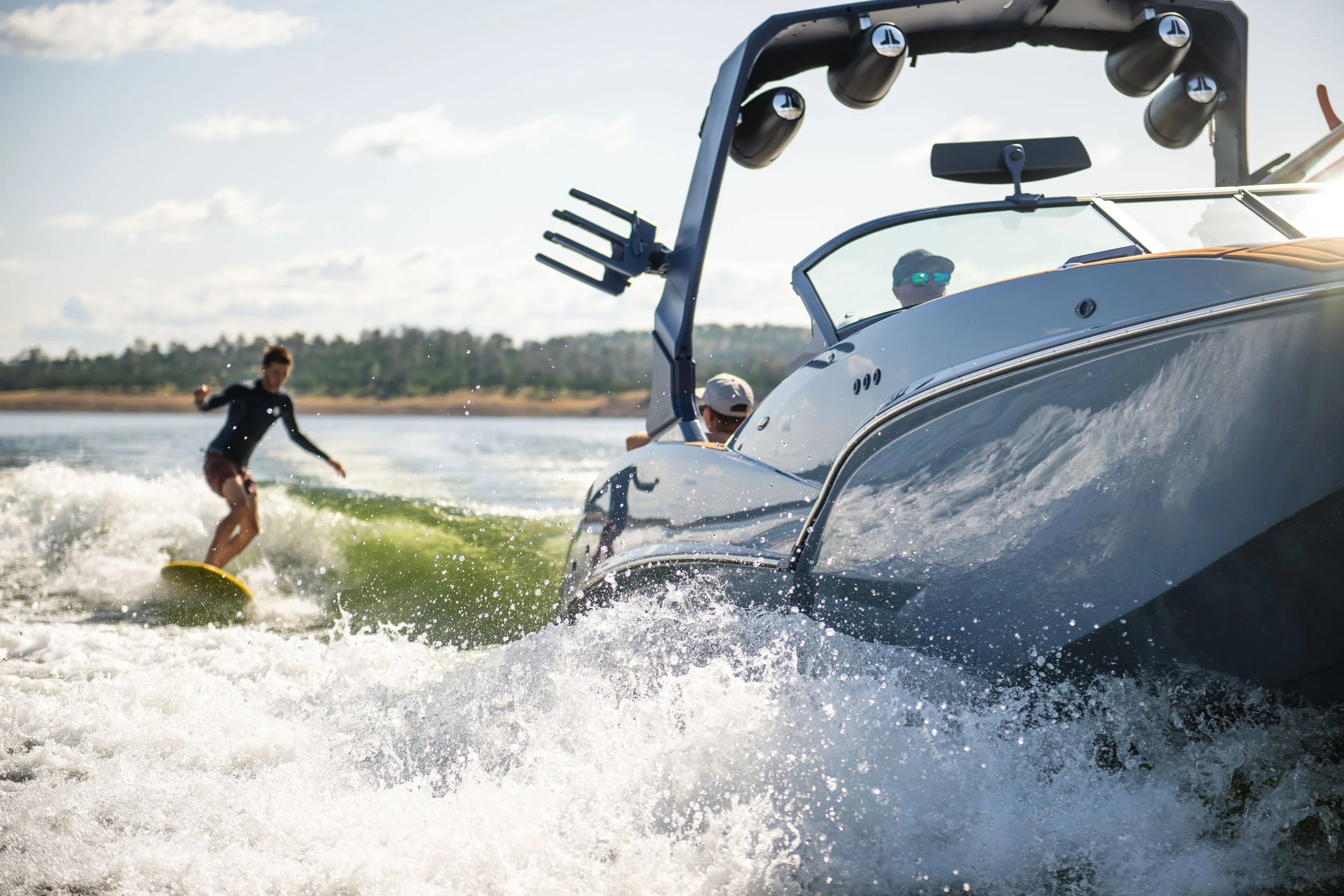 A person wakeboarding behind a motorboat on a lake during sunny weather.