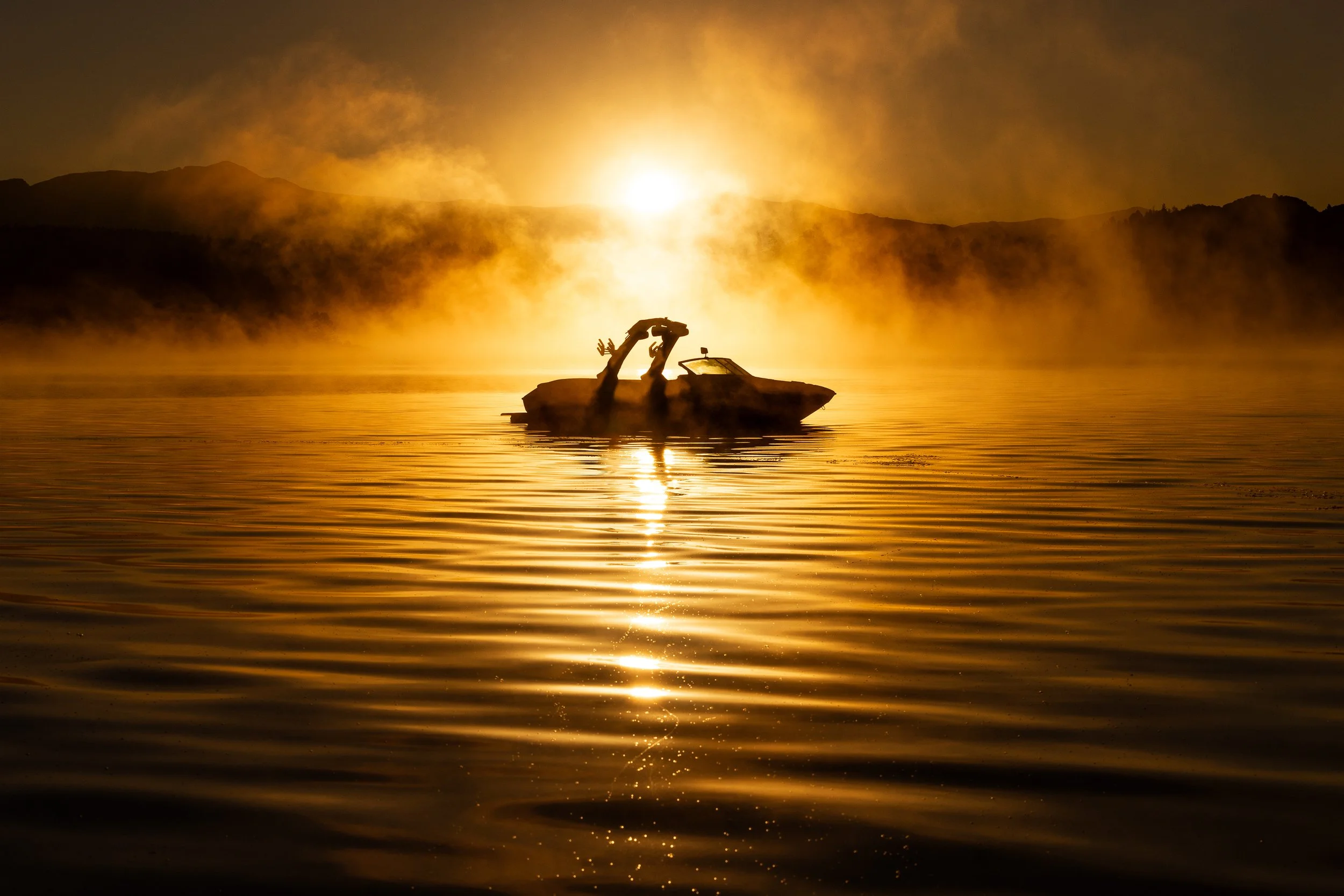 A boat on a calm lake during sunset with the fish tail out of the water, creating a silhouette against the glowing sky