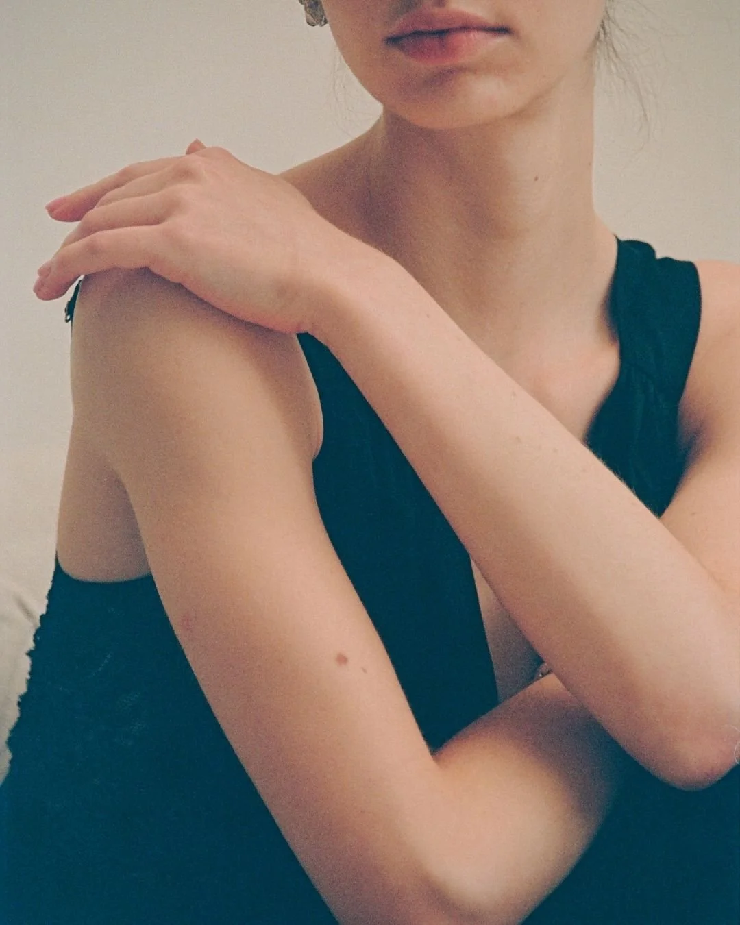 A woman with fair skin, wearing a black sleeveless top, resting her arm on her shoulder, with a neutral facial expression.