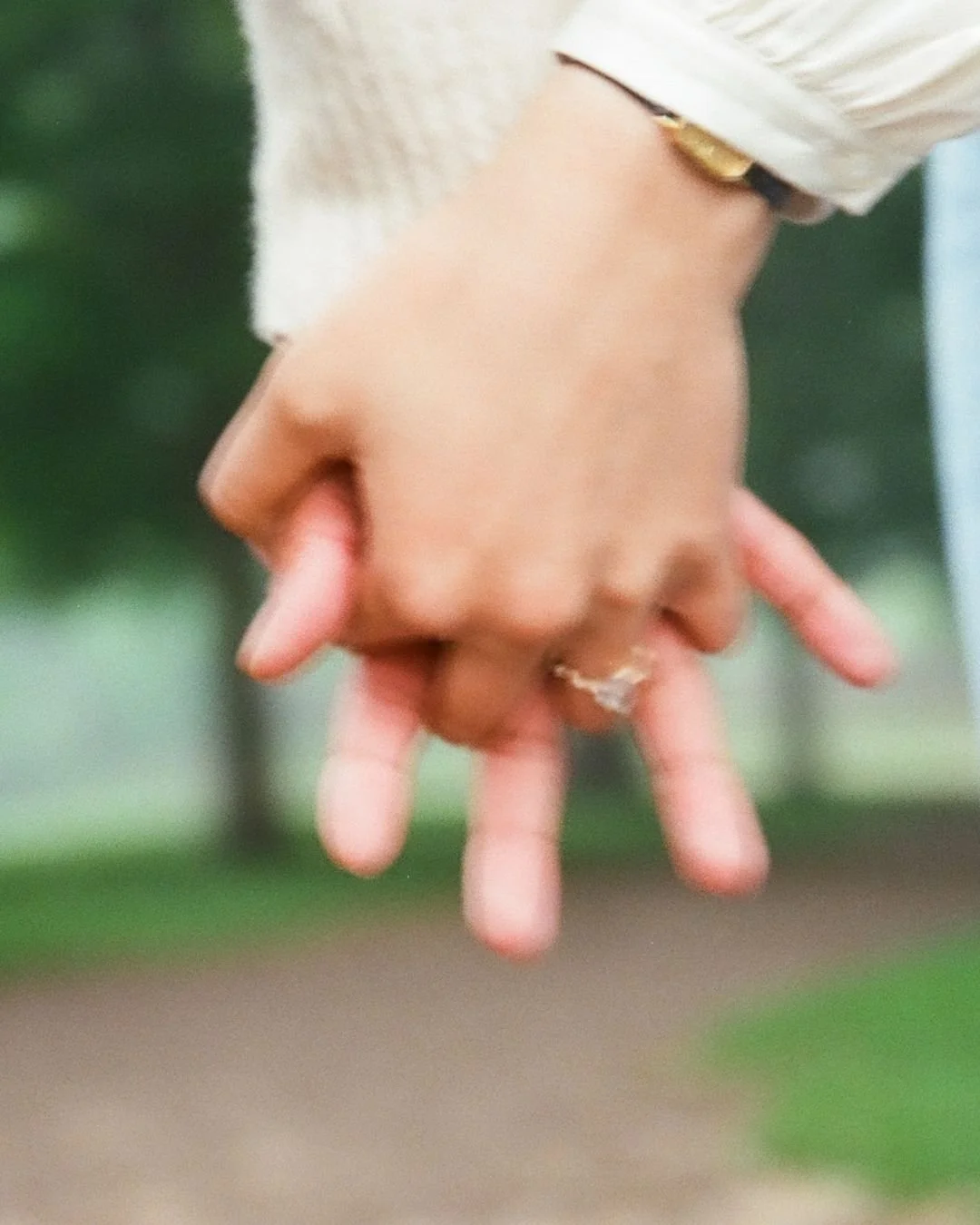 Close-up of a person's hand with fingers spread out, wearing a ring and a watch, against a blurred outdoor background.