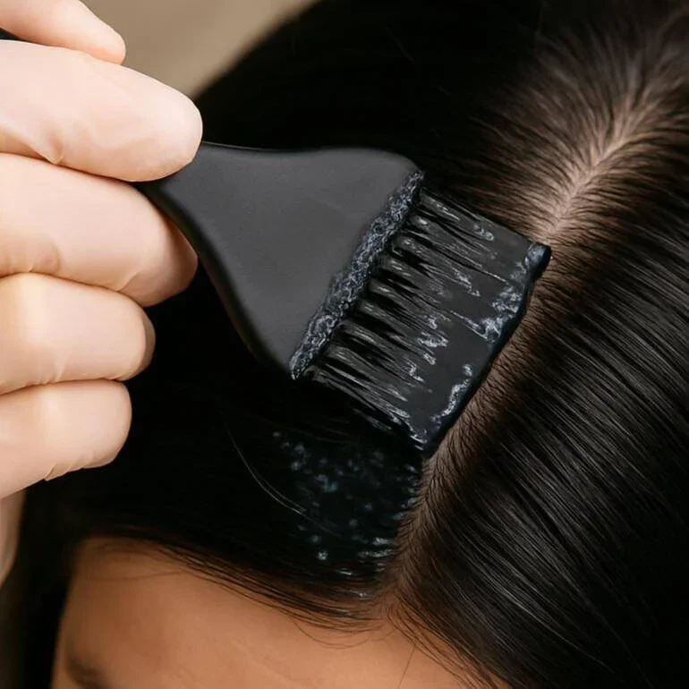 A person using a wide brush to apply hair dye or treatment to the scalp and hair roots.