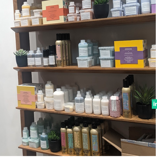 Wooden shelf containing various skincare or cosmetic products in bottles, jars, and boxes, along with small potted succulents.