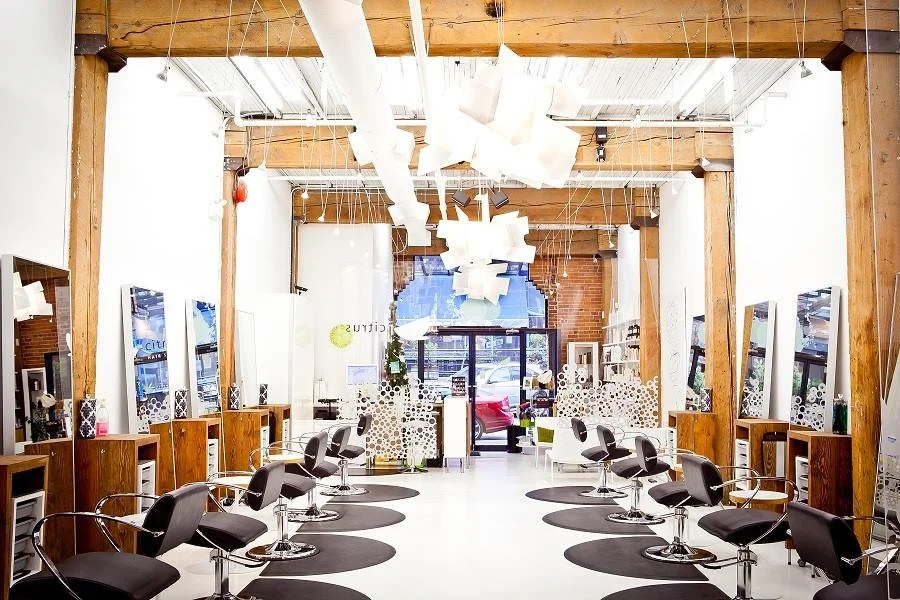 Empty hair salon with stylist chairs, mirrors, and ceiling light fixtures, featuring exposed wooden beams and a storefront window in the background.
