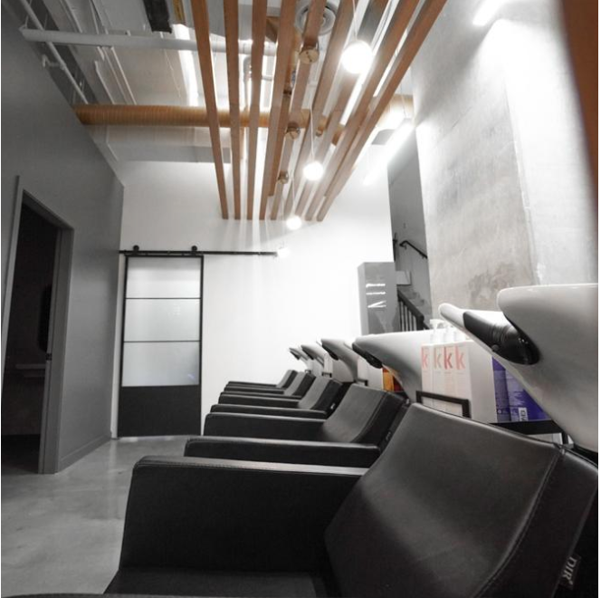 Salon chairs lined up in a modern hair salon with a minimalist design and wooden ceiling accents.