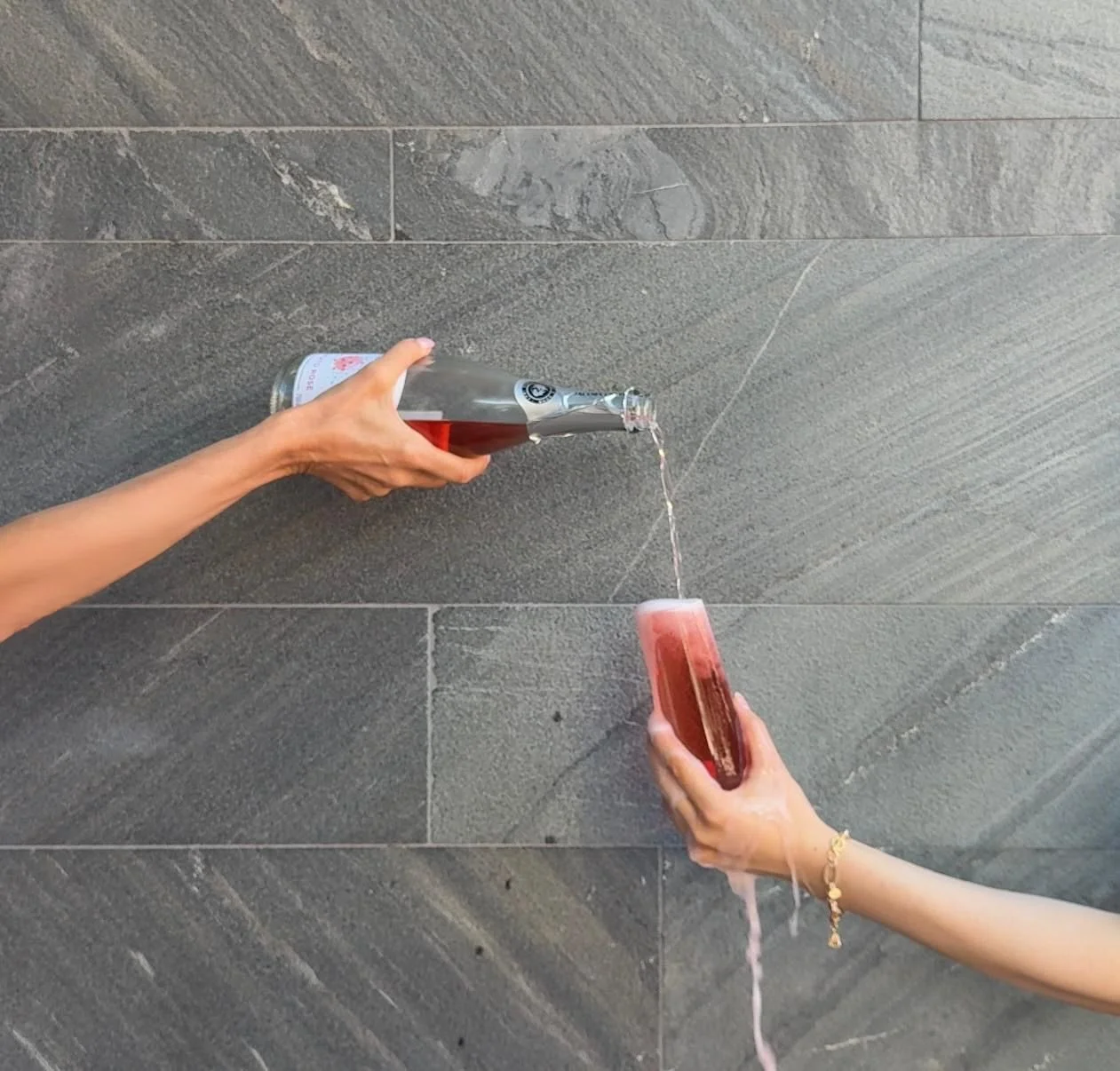 Two people pouring a pink beverage from a bottle into a glass using a tap.