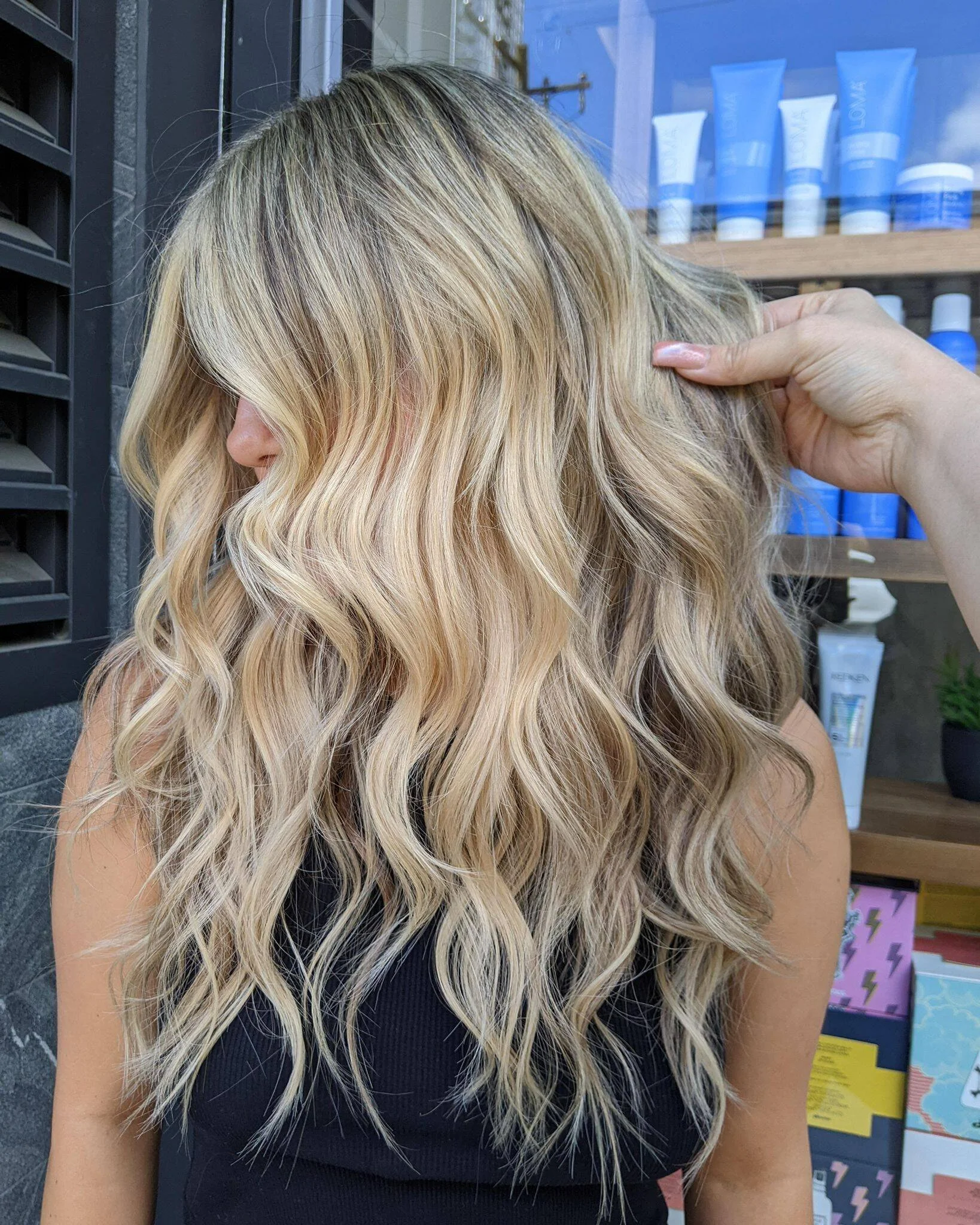 Woman with long, wavy blonde hair, partially covering her face, holding her hair with her hand.