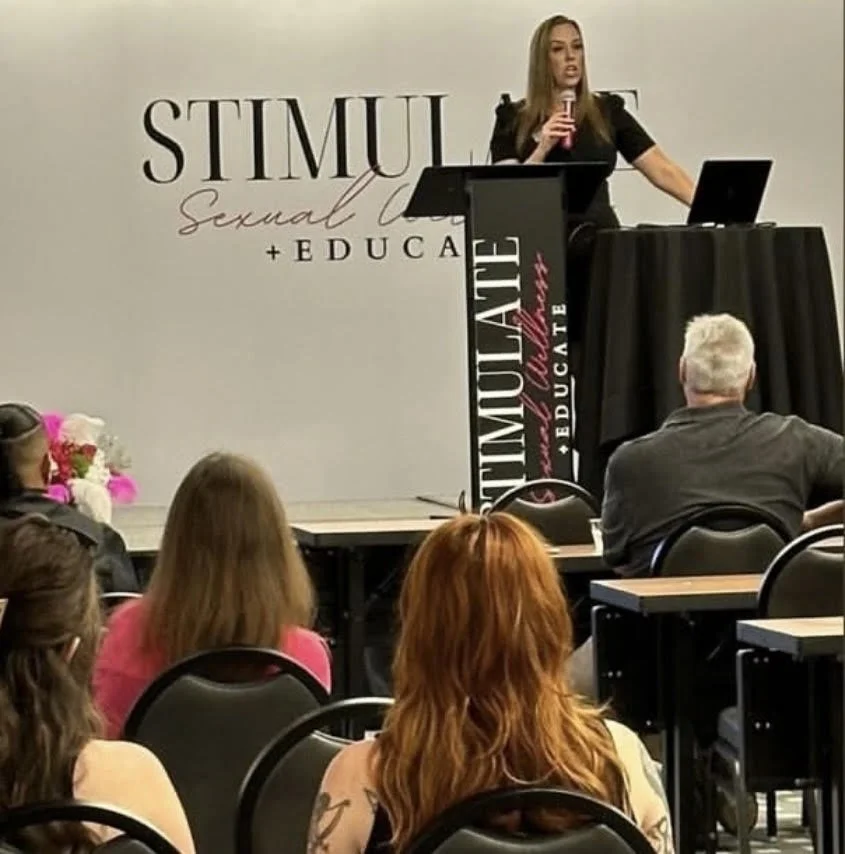 Nicole Leinbach Hoffman giving a presentation at a conference labeled 'Stimul Sexual + Educate' with an audience listening.