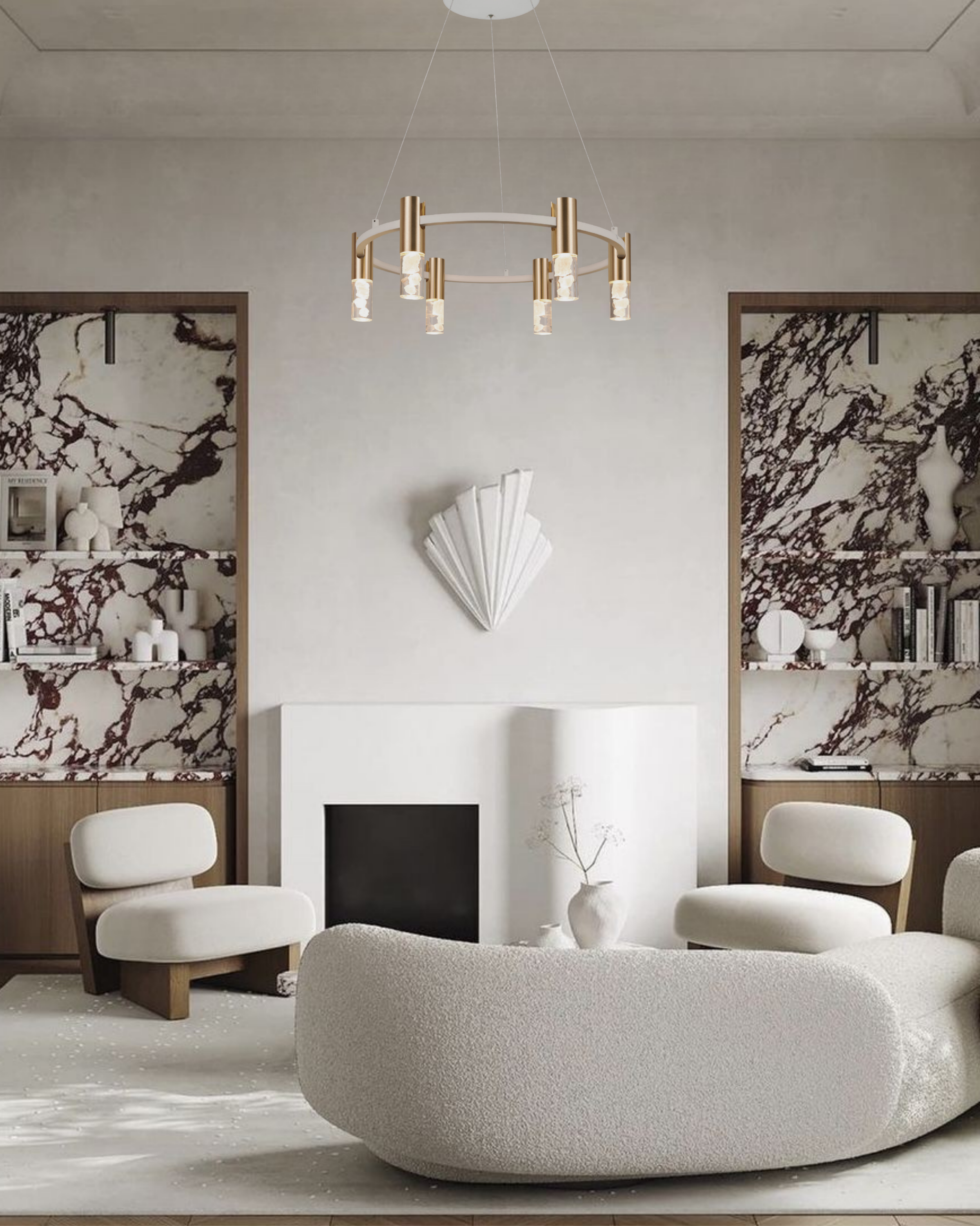 Interior living room with a large, rounded white textured sofa, a white fireplace with a decorative white fan-shaped sculpture above it, and shelves with black and white marble patterned panels and decor, including white vases and books, against light-colored walls.